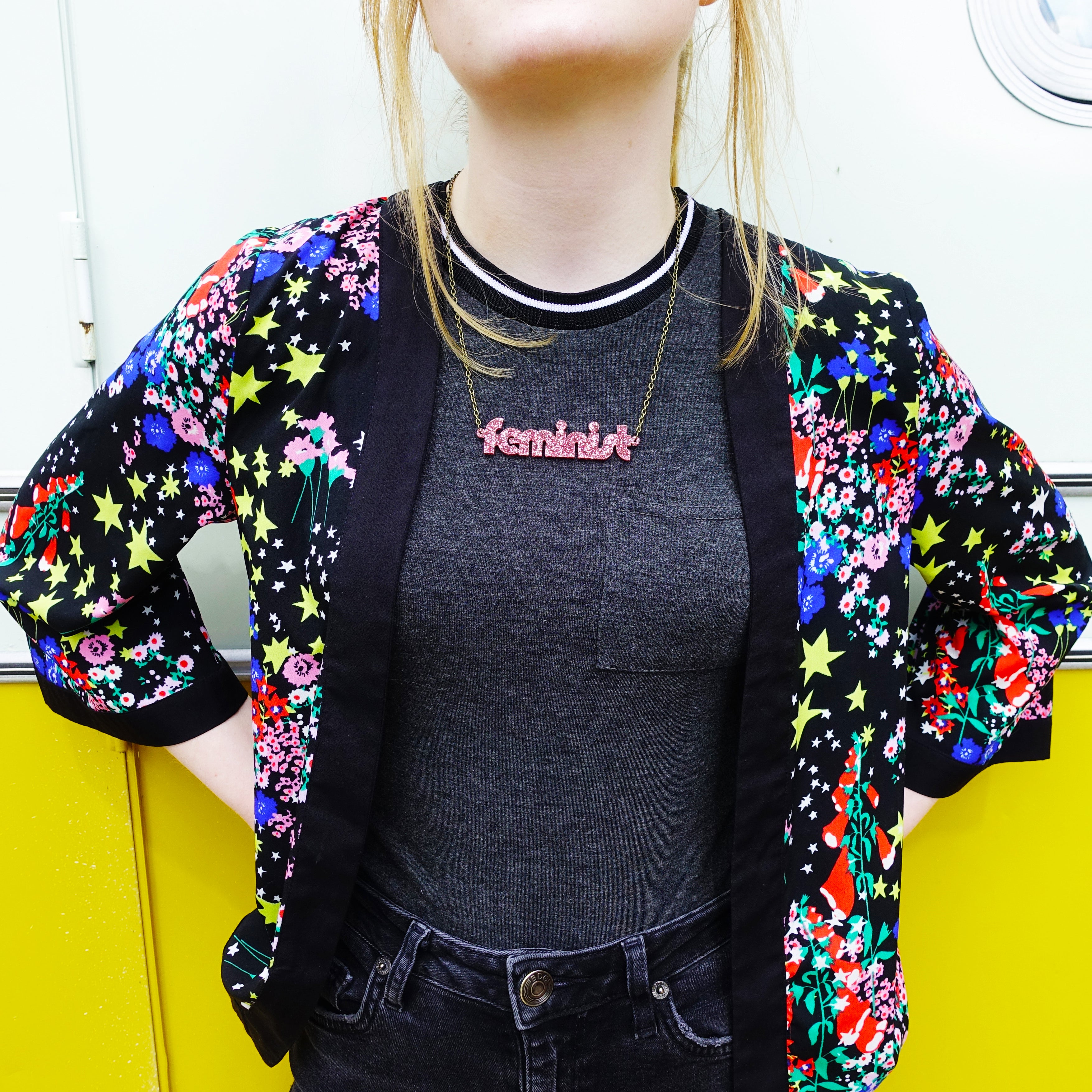 Model wears rose glitter disco font Feminist necklace designed by Sarah Day for Wear and Resist. 