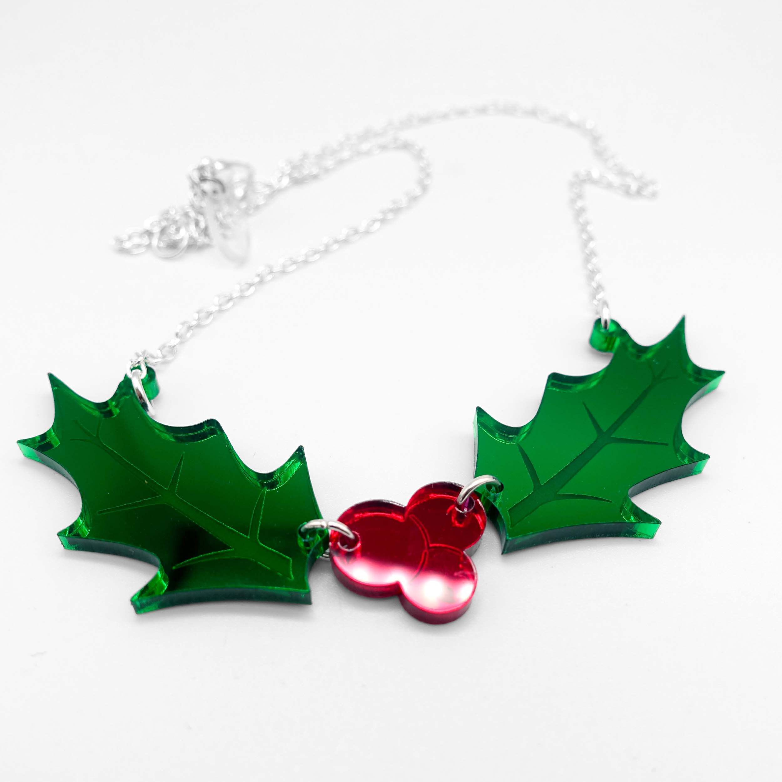 A close up showing the Holly necklace on a silver chain on a white surface. 