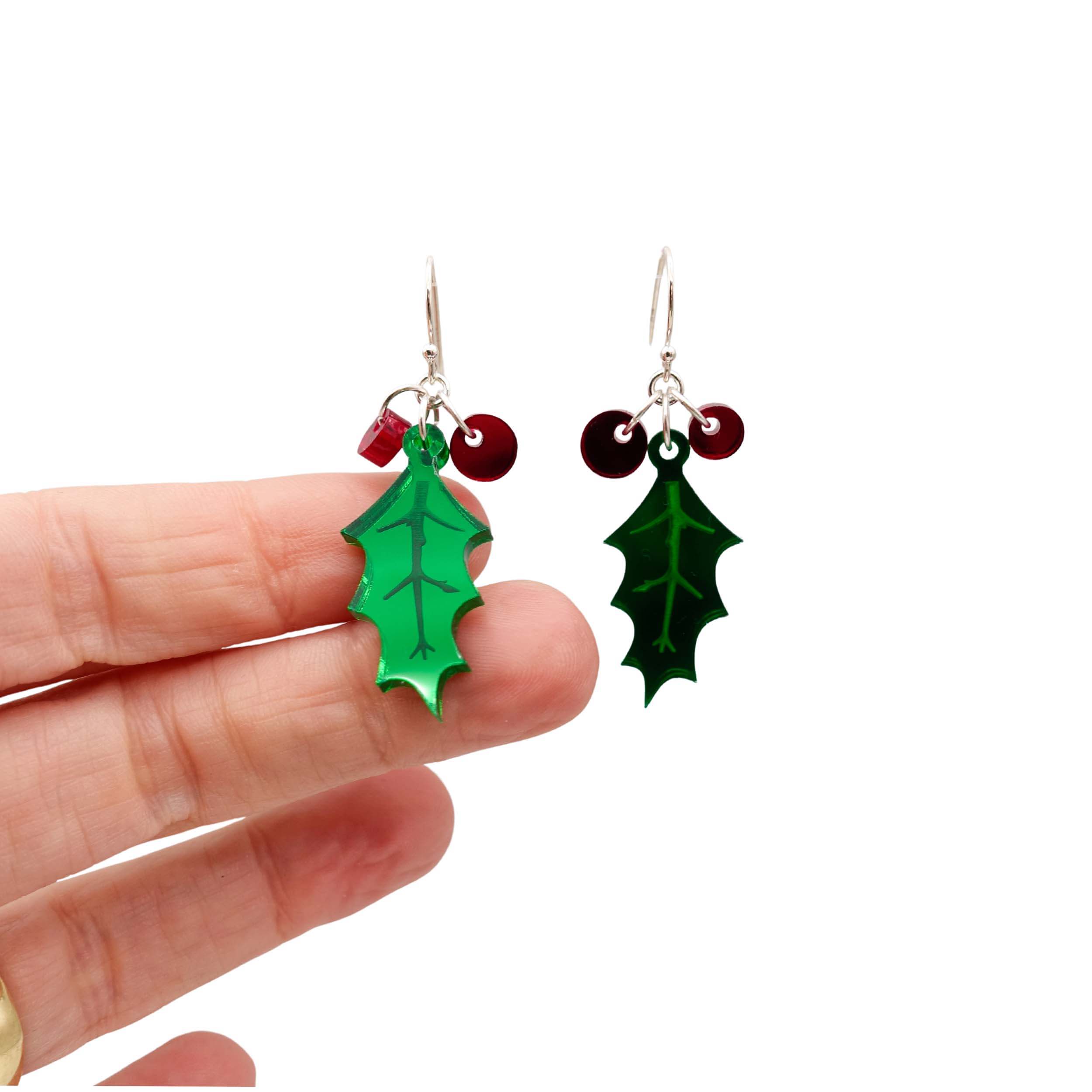 Delicate Holly earrings shown hanging against a white background with my hand for scale, showing the reflective colours of the mirror material. 