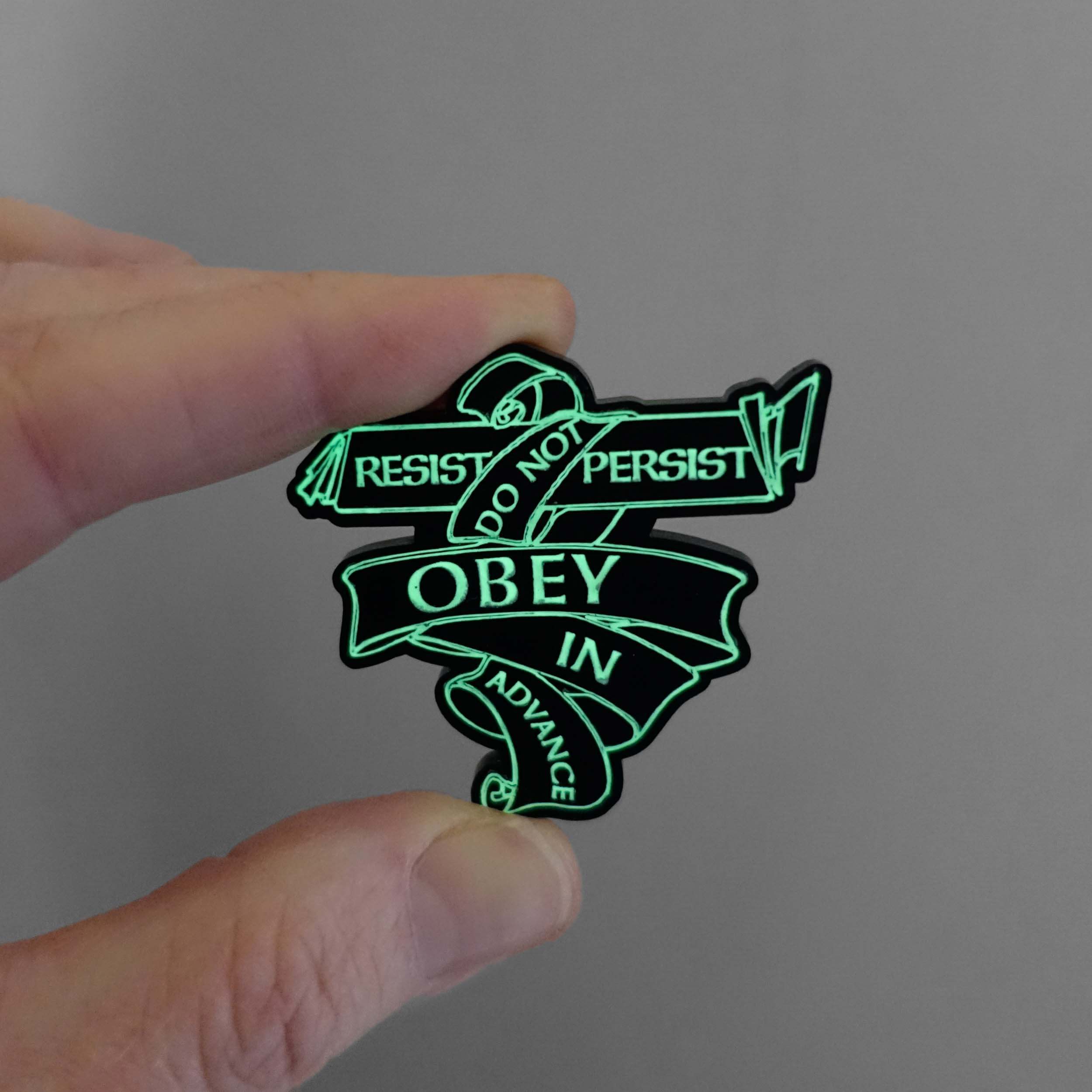 Do Not Obey in Advance, Resist, Persist pin etched in glow-in-the-dark pigment shown glowing in the dark. £2 goes to the ACLU Freedom Defense Fund. 