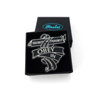 Do Not Obey in Advance, Resist, Persist pin etched in glow-in-the-dark pigment, shown in a small Wear and Resist gift box. 