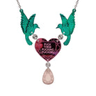 A mirror acrylic necklace with two green birds holding a pink heart that says 'F*ck these F*cking F*ckers' with a rose gold 'jewel' hanging from the centre. 