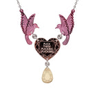 A mirror acrylic necklace with two pink birds holding a rose-gold heart that says 'F*ck these F*cking F*ckers' with a gold 'jewel' hanging from the centre. 