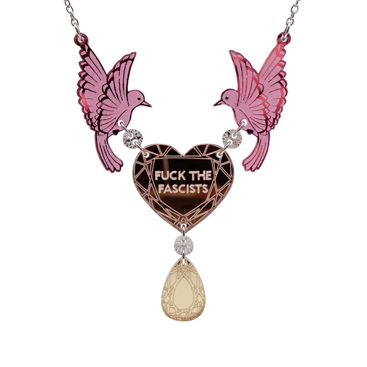 A mirror acrylic necklace with two pink birds holding a rose-gold heart that says 'F*ck the Fascists' with a gold 'jewel' hanging from the centre. 