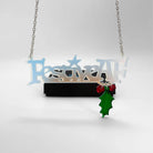 Festive AF matte iridescent necklace with hanging holly leaf and berries, shown hanging in front of a Wear and Resist gift box. 
