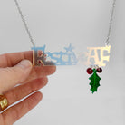 Festive AF matte iridescent necklace with hanging holly leaf and berries, shown hanging catching the light with my hand holding it for scale. 