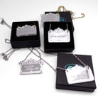 A group of delicate etched necklaces etched with rude and sweary words shown in and on Wear & Resist small gift boxes. 