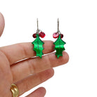 Naturalistic Holly earrings with red berries shown hanging on stainless steel ear wires against a white background with my hand behind for scale. 