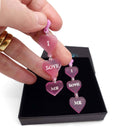 I Love Me heart drop earrings in pale pink frost shown being held up from a Wear and Resist gift box. 