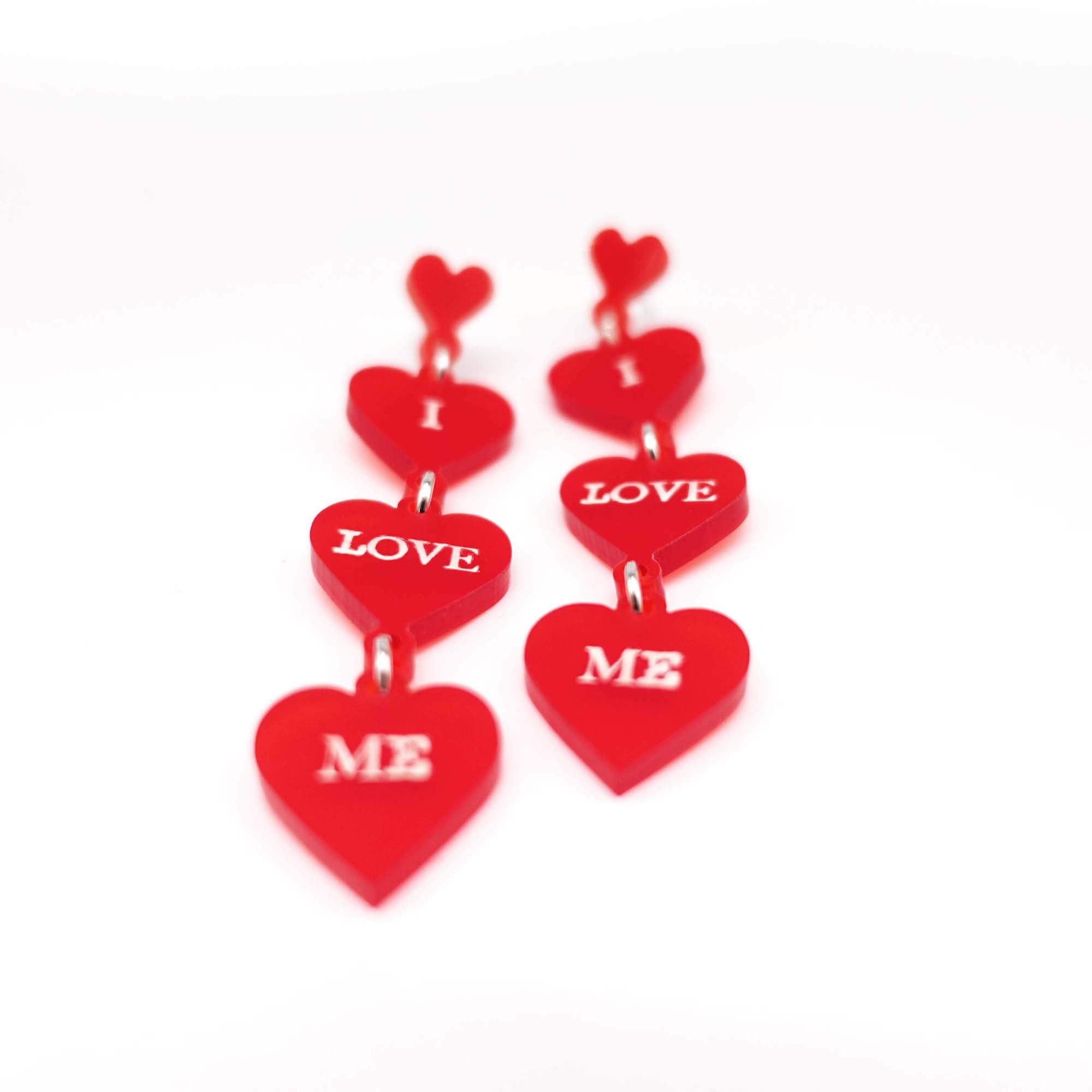 I Love Me heart drop earrings in chilli red frost with glow-in-the-dark etched words, shown on a white background.