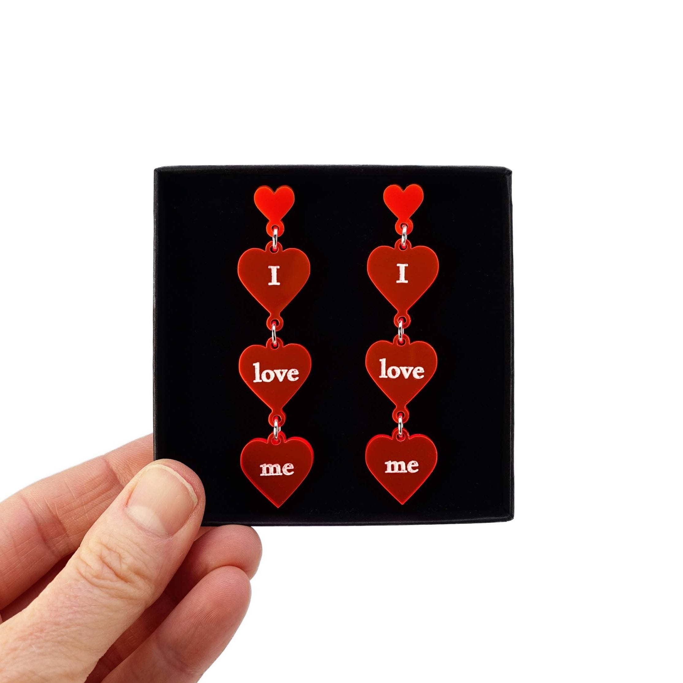 I love me heart drop earrings in hot red shown held up in a Wear and Resist gift box. 