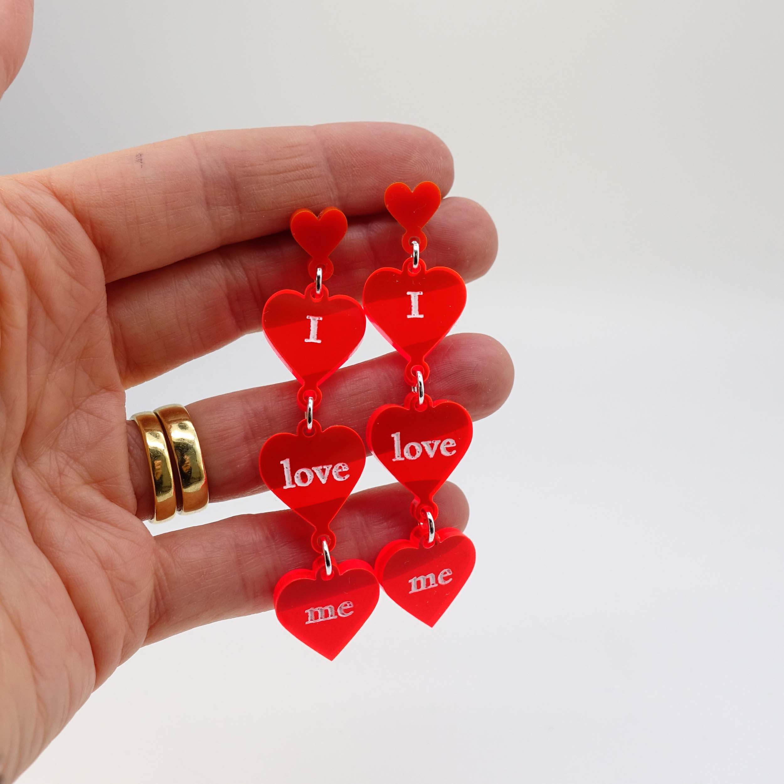 I love me heart drop earrings in hot red shown held up for scale. 