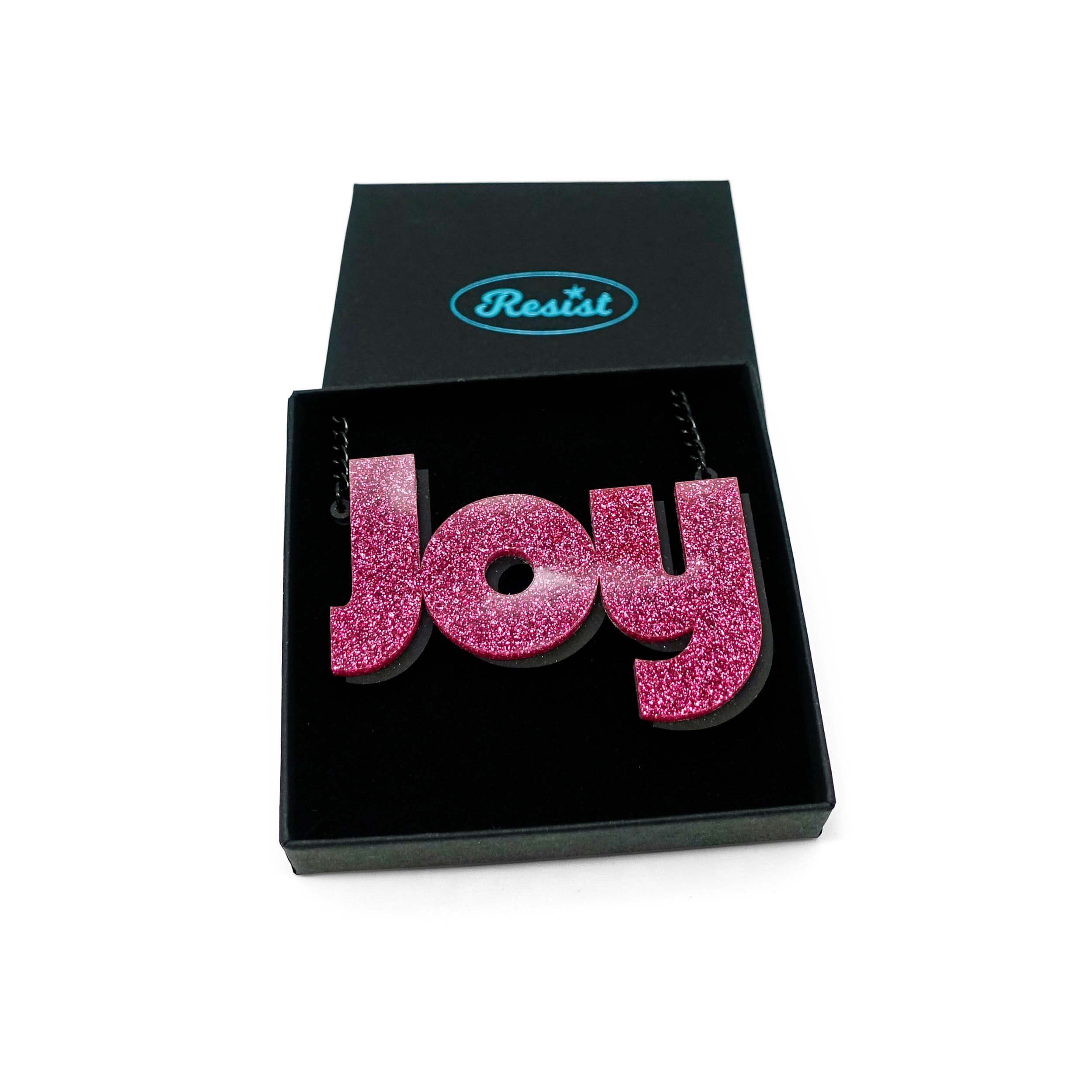 Joy statement necklace in pink glitter, shown in a Wear and Resist gift box. 