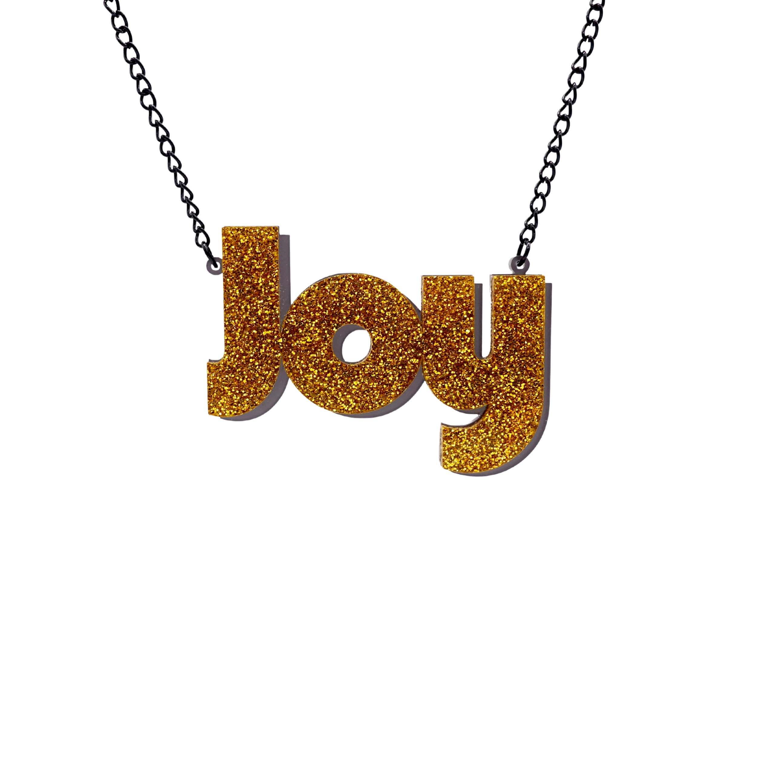 Joy statement necklace in ultra gold glitter, with slate frost drop shadow backing layer. Shown hanging against a white background. 