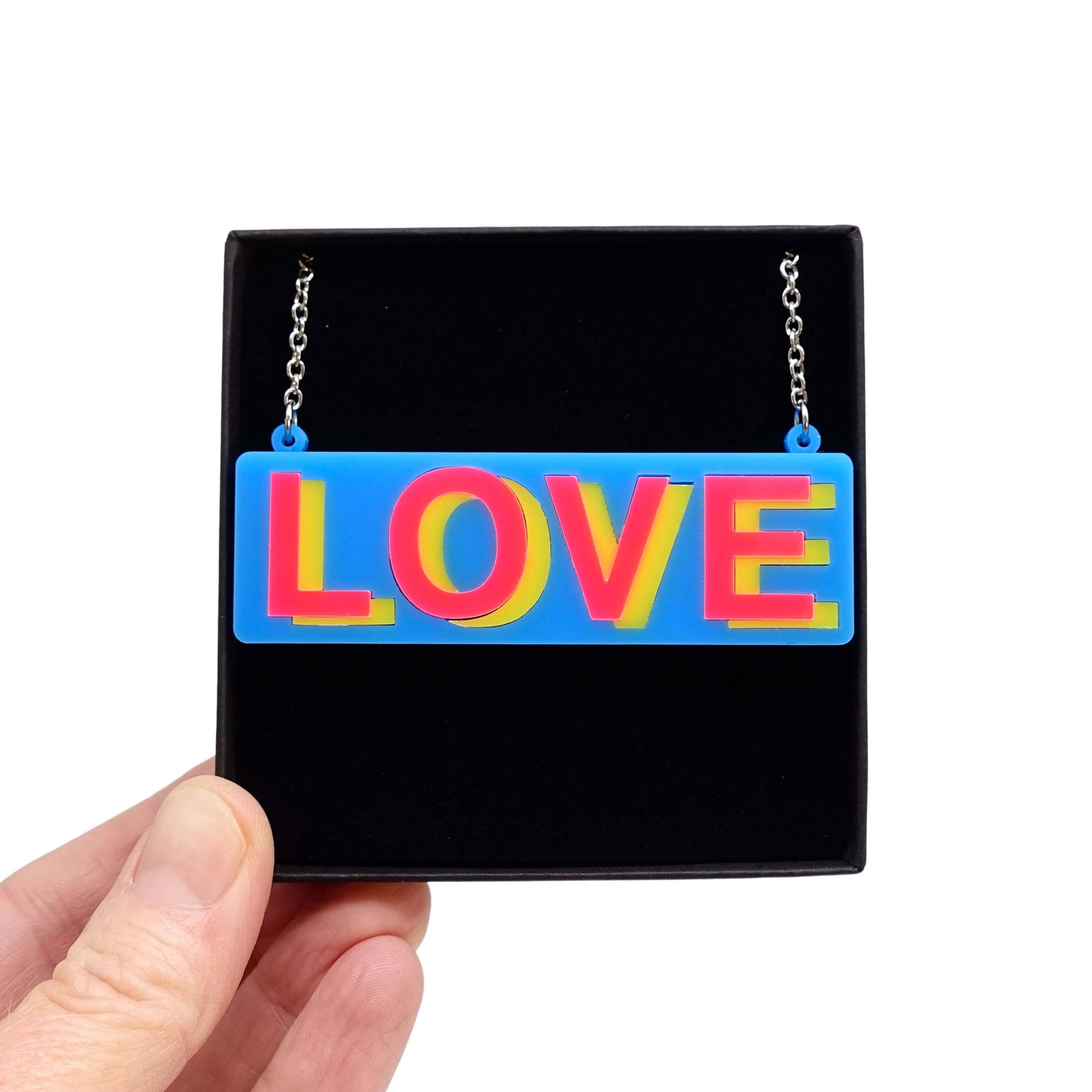 LOVE necklace in colourful blue, hot pink and yellow, shown held up in a Wear and Resist gift box. 