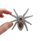 Sarah's fingers hold up the All Hail Lady Hail Spider brooch against a white background. 