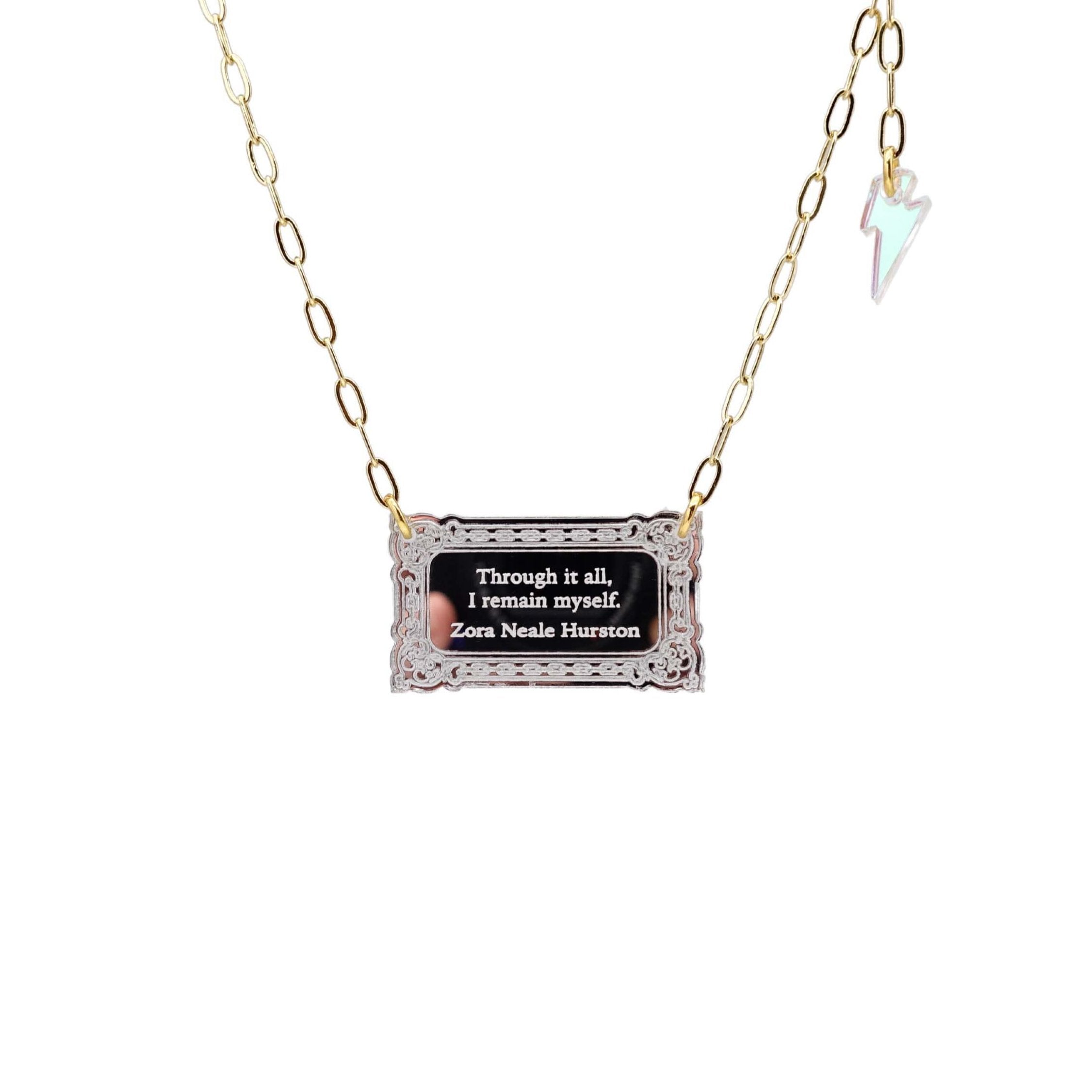 Literary Quote necklace etched with a quote by Zora Neale Hurston, 'Through it all, I am myself.' Shown on a gold plated paperclip chain finished with an iridescent lightning bolt, hanging against a white background. 