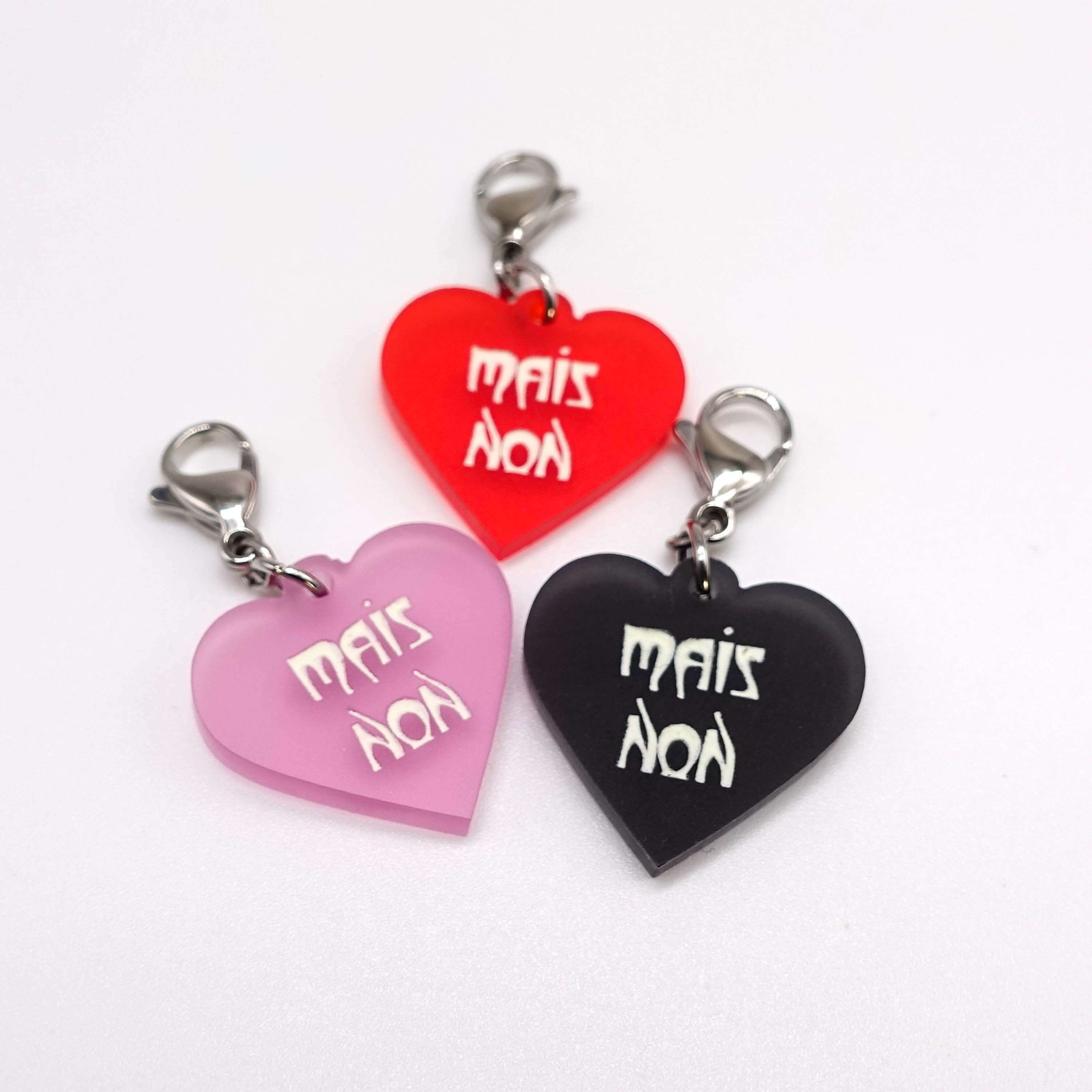 Heart charms etched and hand-painted with the words Mais Non in glow in the dark pigment. 