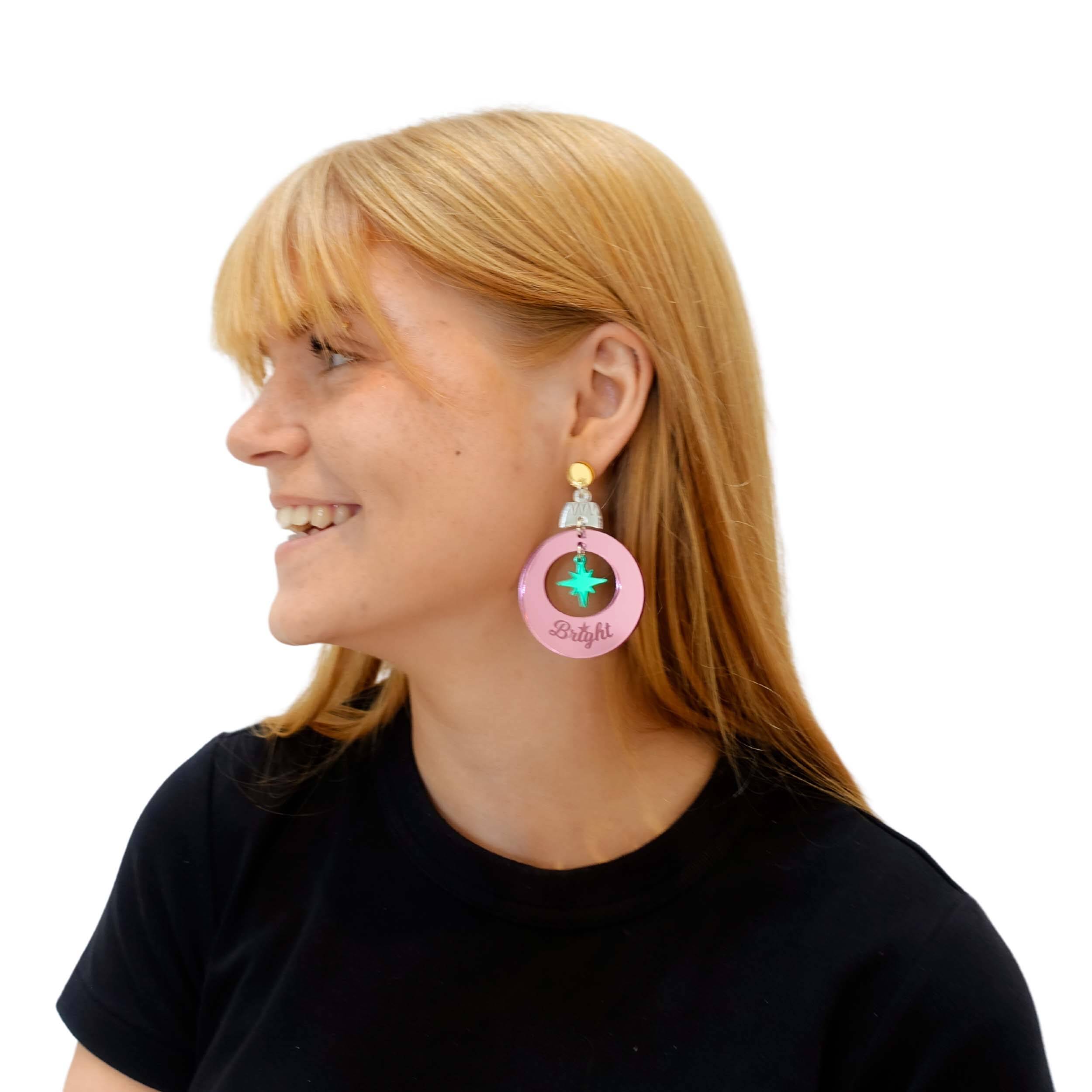 Eliza wears Merry & Bright Christmas bauble earrings in electric green and pink mirror. 