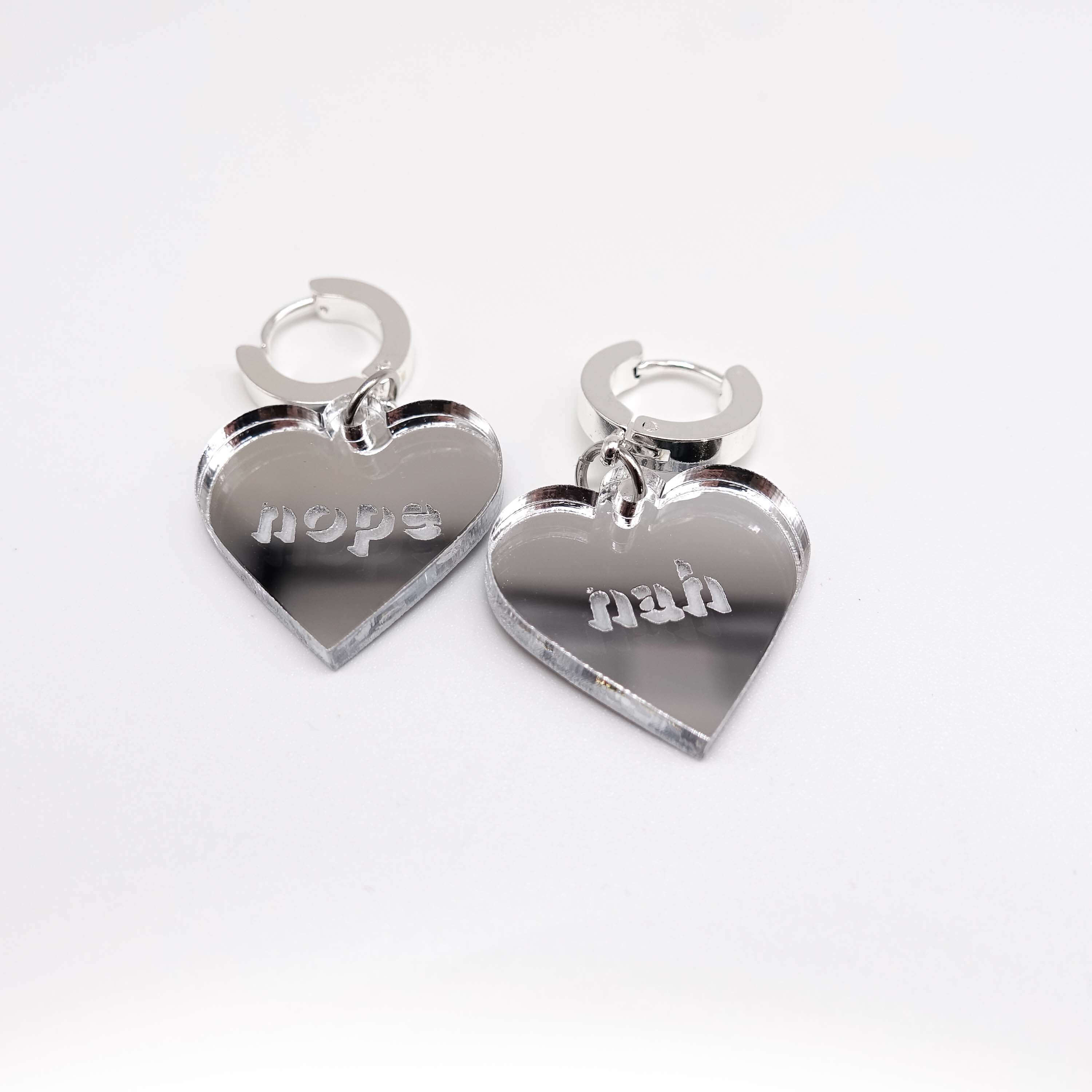 Nah Nope heart shaped huggie hoop earrings in silver mirror shown sitting on a white surface. 