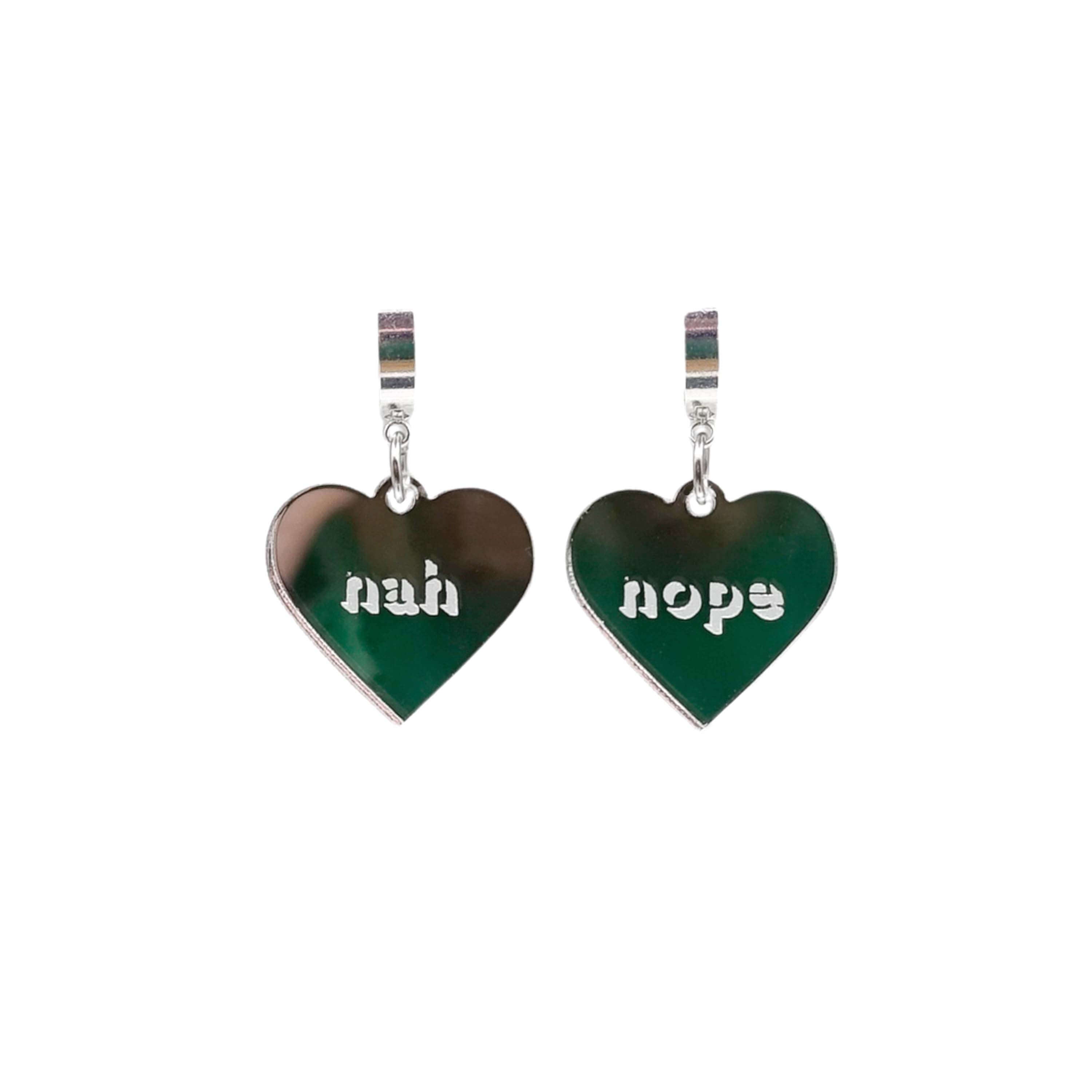 Nah Nope heart shaped huggie hoop earrings in silver mirror shown hanging against a white background. 