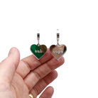 Nah Nope heart shaped huggie hoop earrings in silver mirror shown hanging against a white background with my hand behind for scale. 