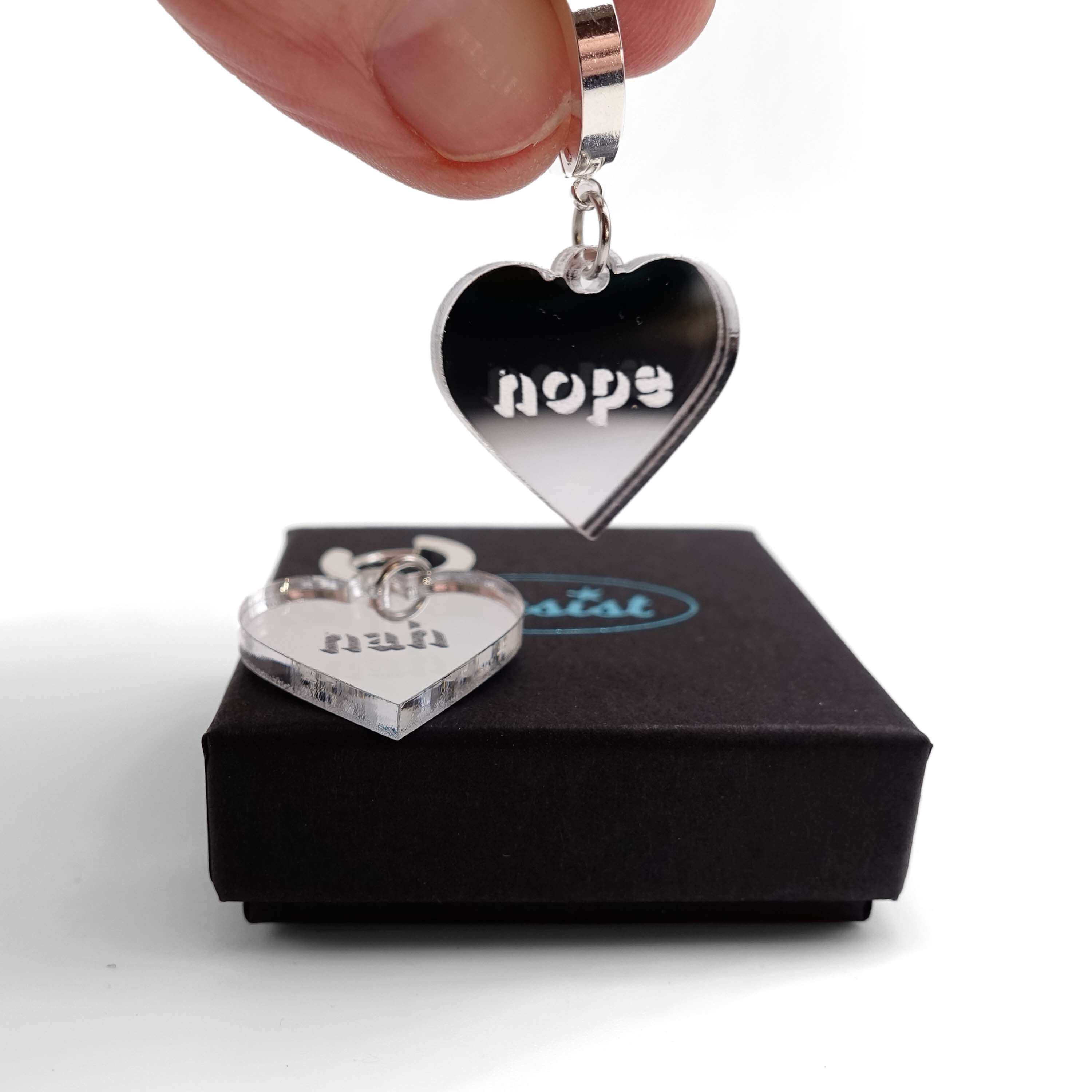 Nah Nope heart shaped huggie hoop earrings in silver mirror with me holding the Nah earring. 