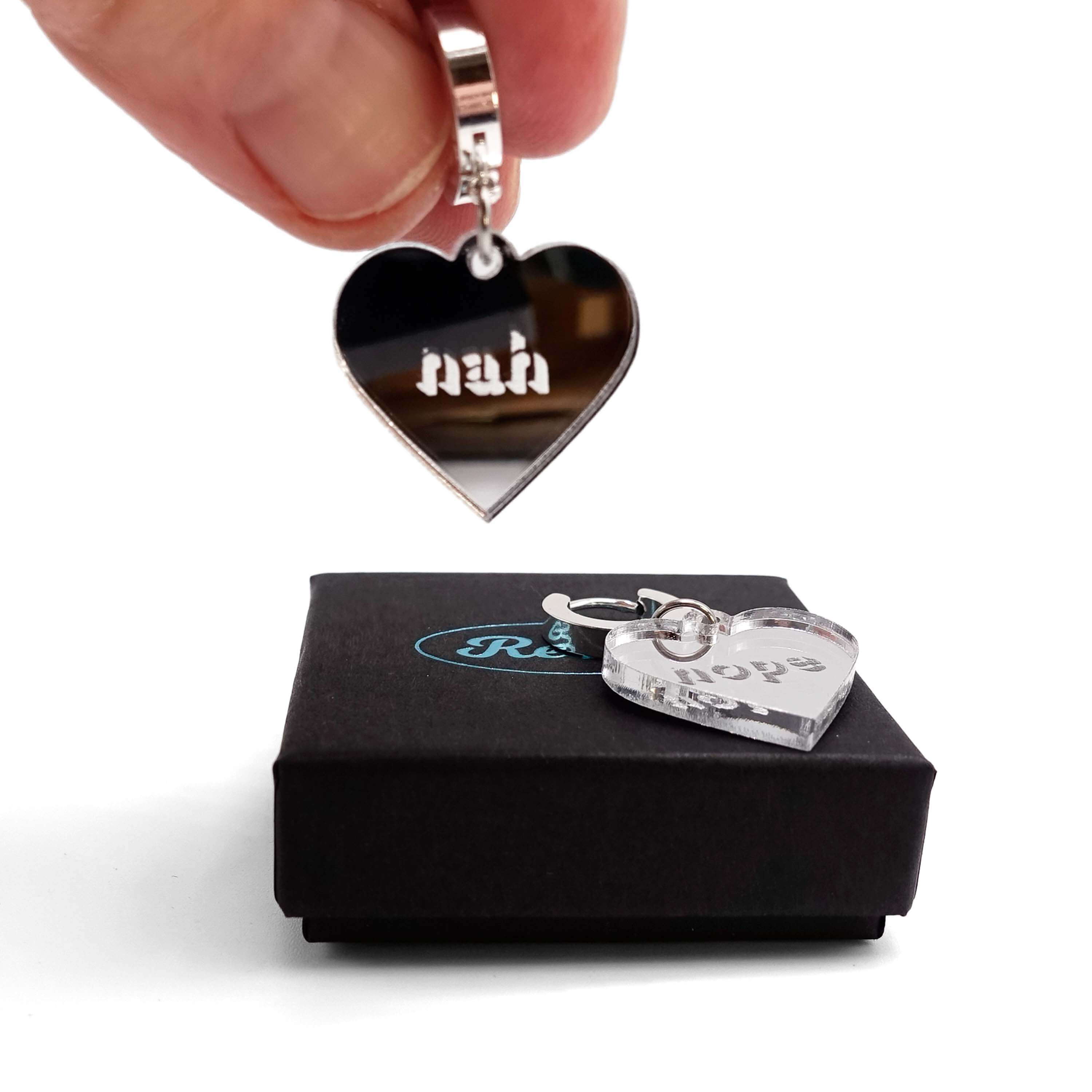 Nah Nope heart shaped huggie hoop earrings in silver mirror with me holding the Nope earring. 