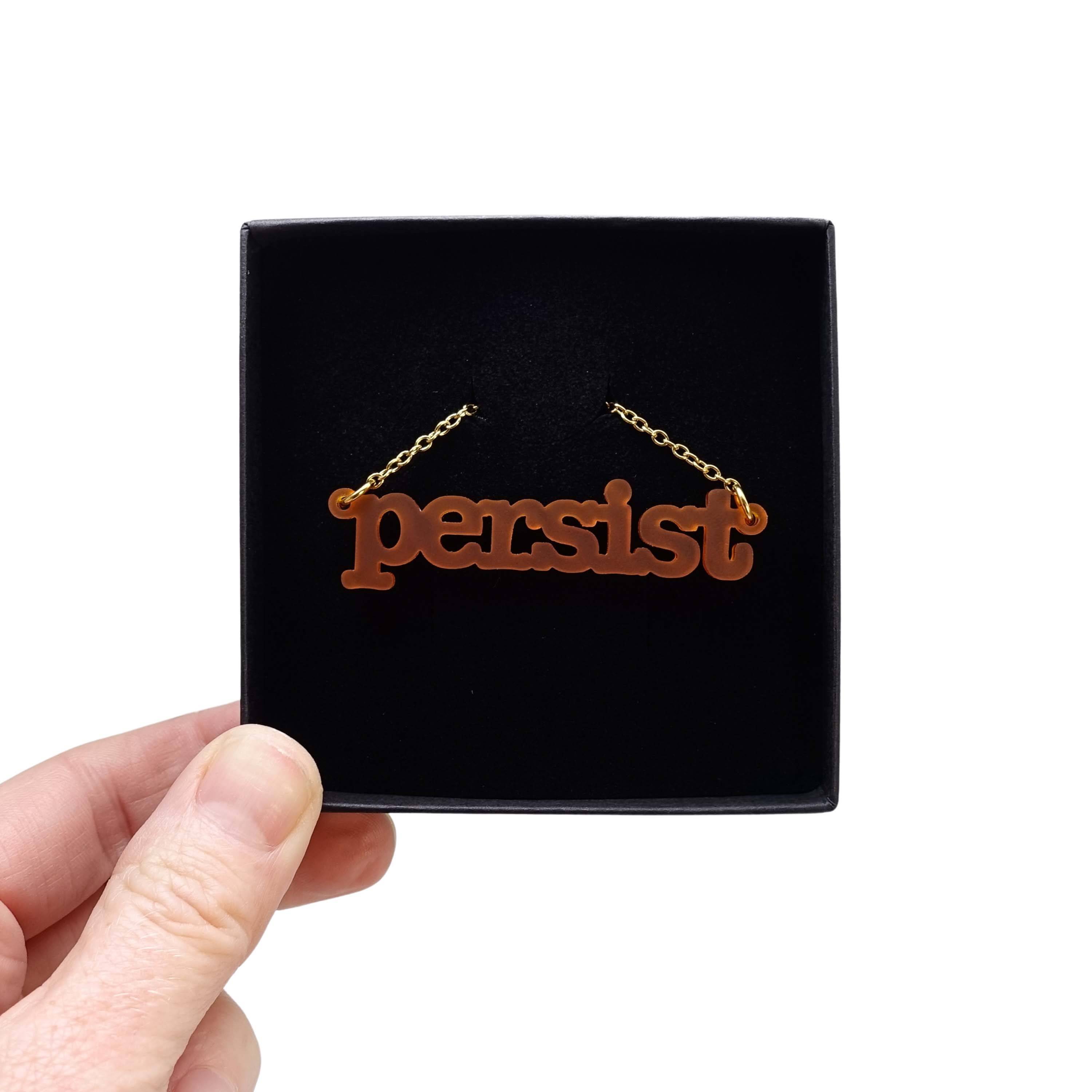 Typewriter Resist necklace in cider frost shown held up in a Wear and Resist gift box.