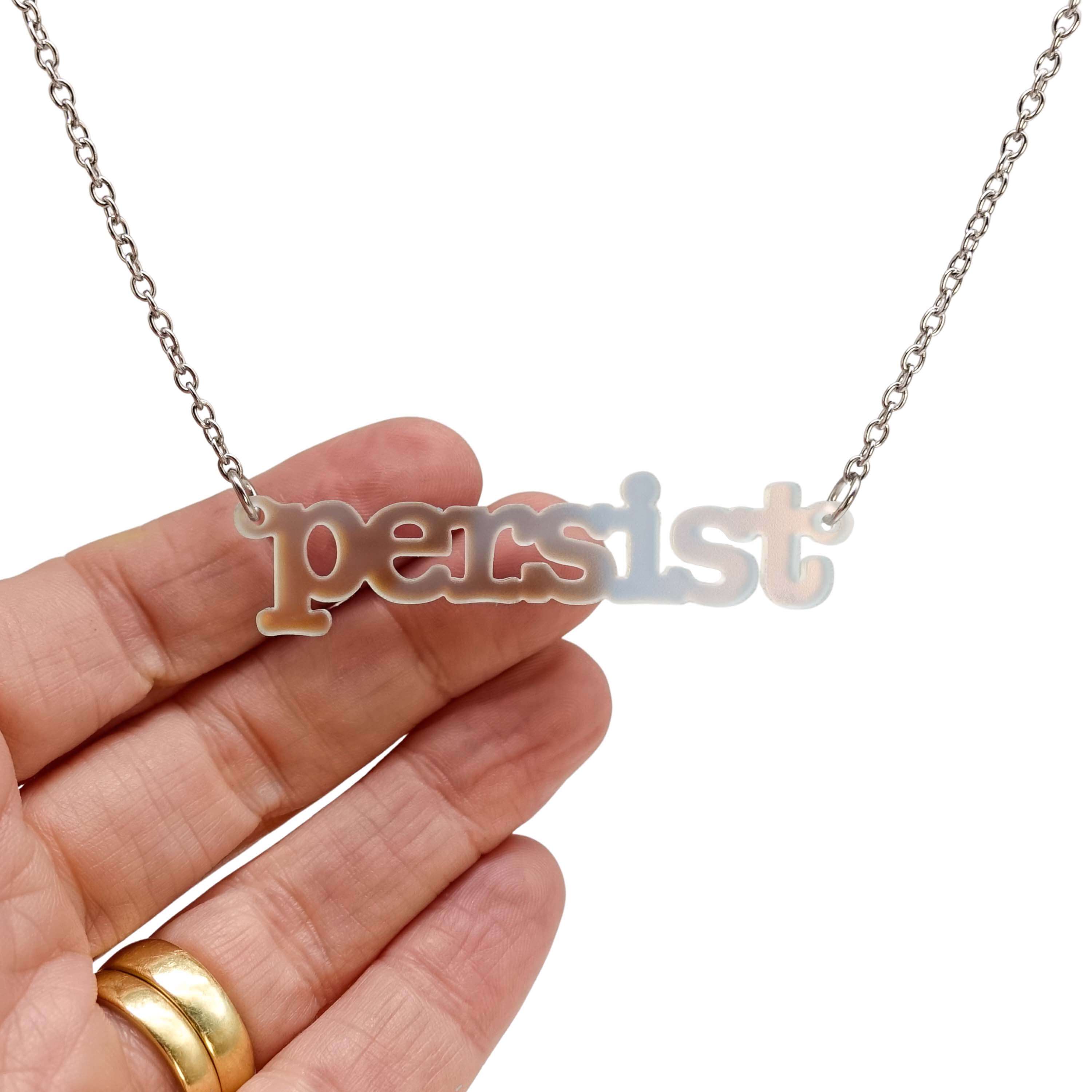 Typewriter Resist necklace in matte iridescent shown hanging on a stainless steel chain against a white background, with my hand behind to show the transparency of the material. 