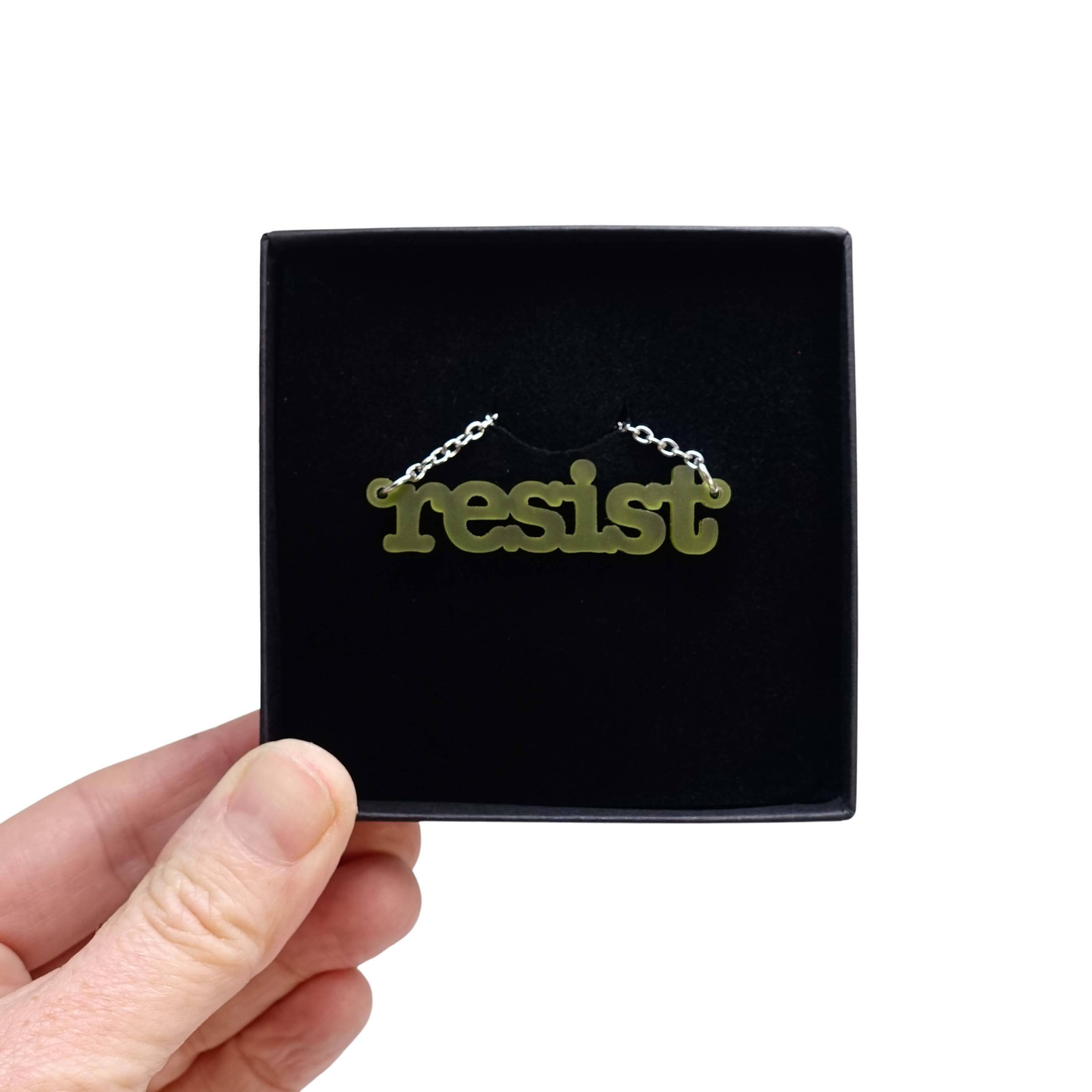 Typewriter Resist necklace in olive frost shown held up in a Wear and Resist gift box. 