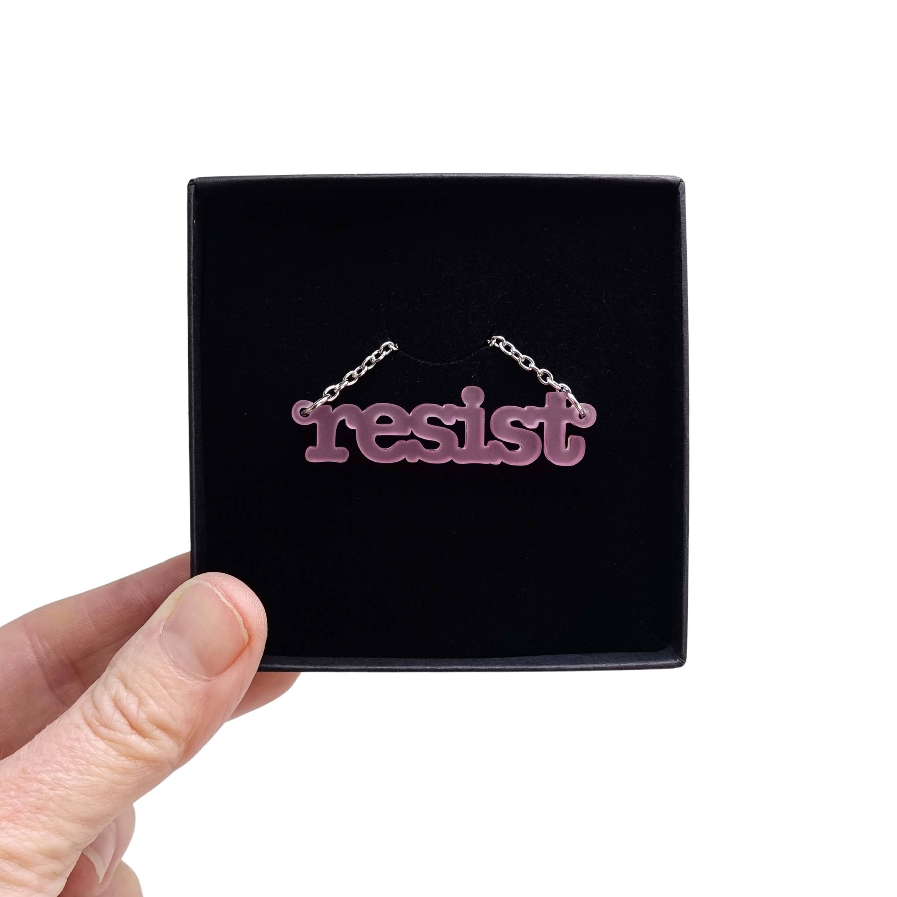 Typewriter Resist necklace in pink frost shown held up in a Wear and Resist gift box. 