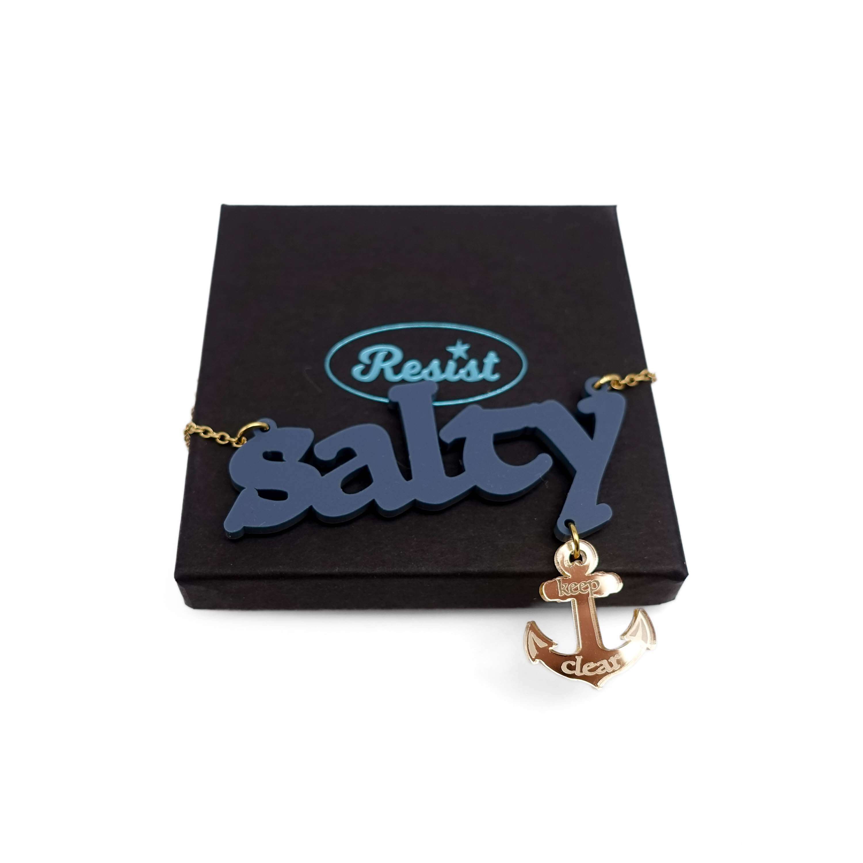 Salty necklace with an etched anchor that says 'keep clear' shown on a gold-plated stainless steel chain on a Wear and Resist gift box.
