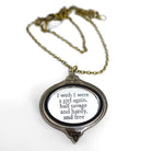 'I wish I were a girl again' Wuthering Heights necklace from the Bronte Collection, in etched mirror acrylic on an antique gold chain, shown sitting on a white surface. 