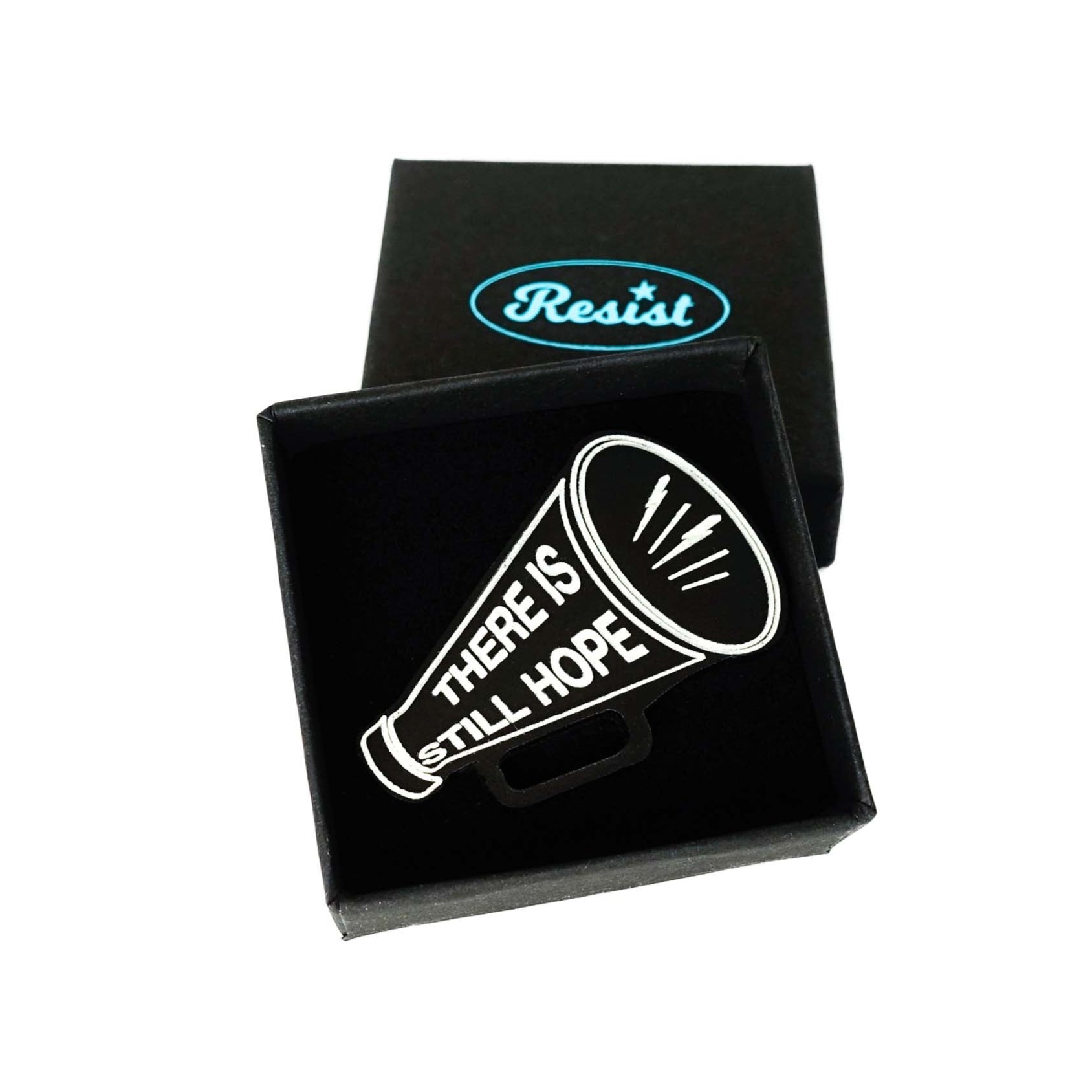 Matte black small megaphone brooch etched in glow-in-the-dark pigment with the words There is Still Hope. Shown in a small Wear and Resist gift box. 