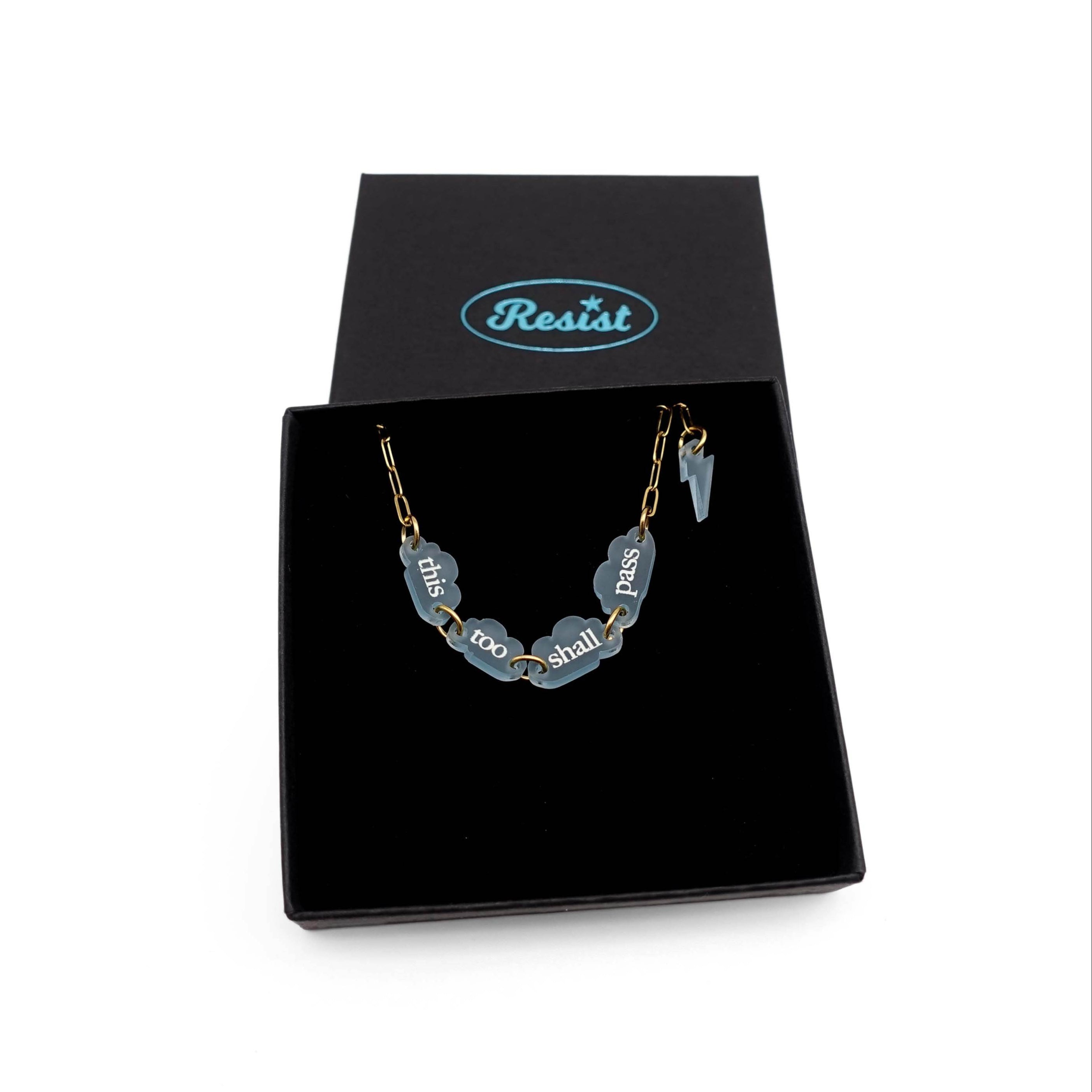 This too shall pass bracelet with words etched in glow-in-the-dark pigment on small clouds on a gold-plated stainless steel chain, show in a Wear and Resist gift box. 