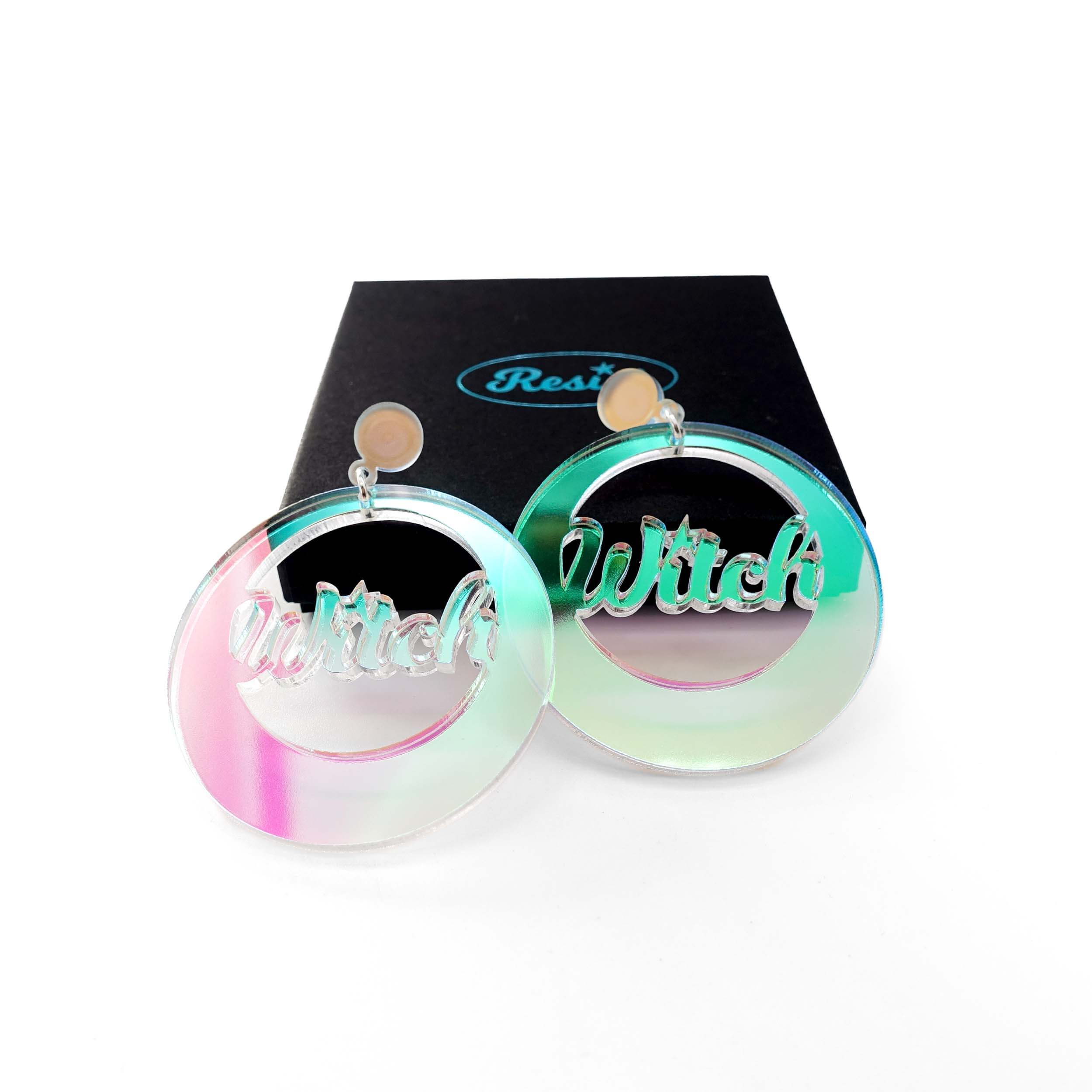 A pair of Witch iridescent hoop earrings, shown with a Wear and Resist gift box. 