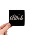 B*tch necklace in siver glitter, shown in a Wear and Resist gift box being held up. 