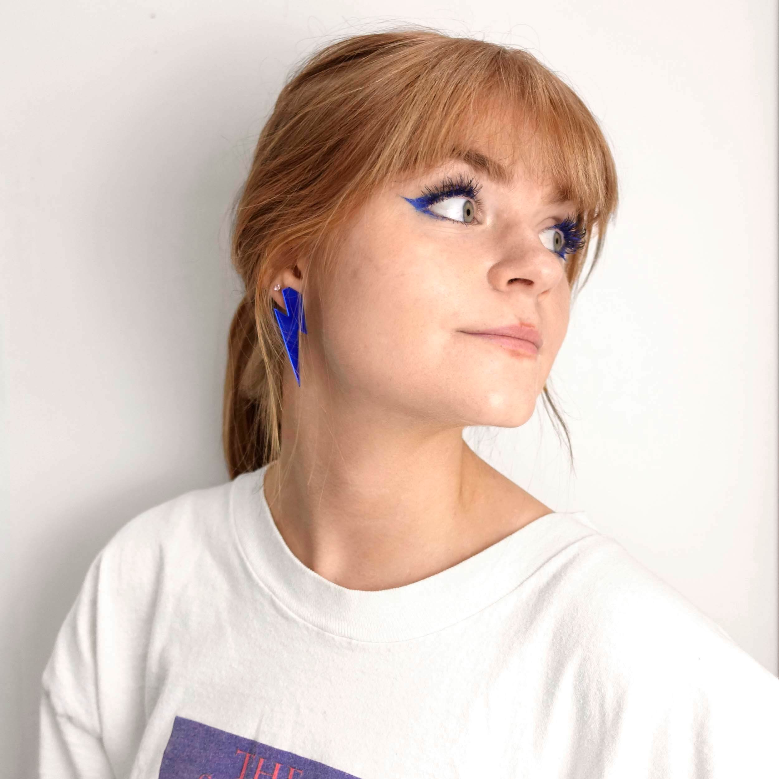 Model wears large Lightning bolt earrings in electric blue mirror. 