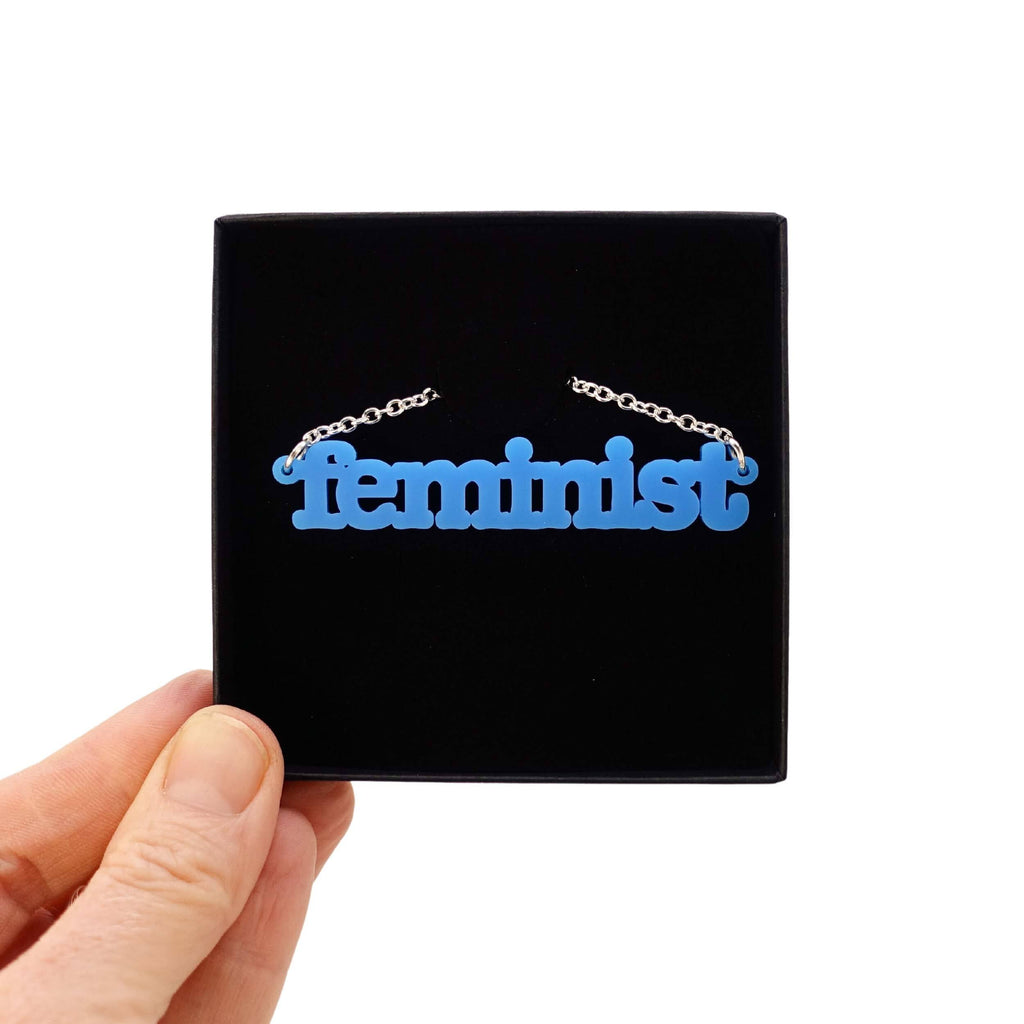 Bright blue Feminist necklace shown in a Wear and Resist gift box. 