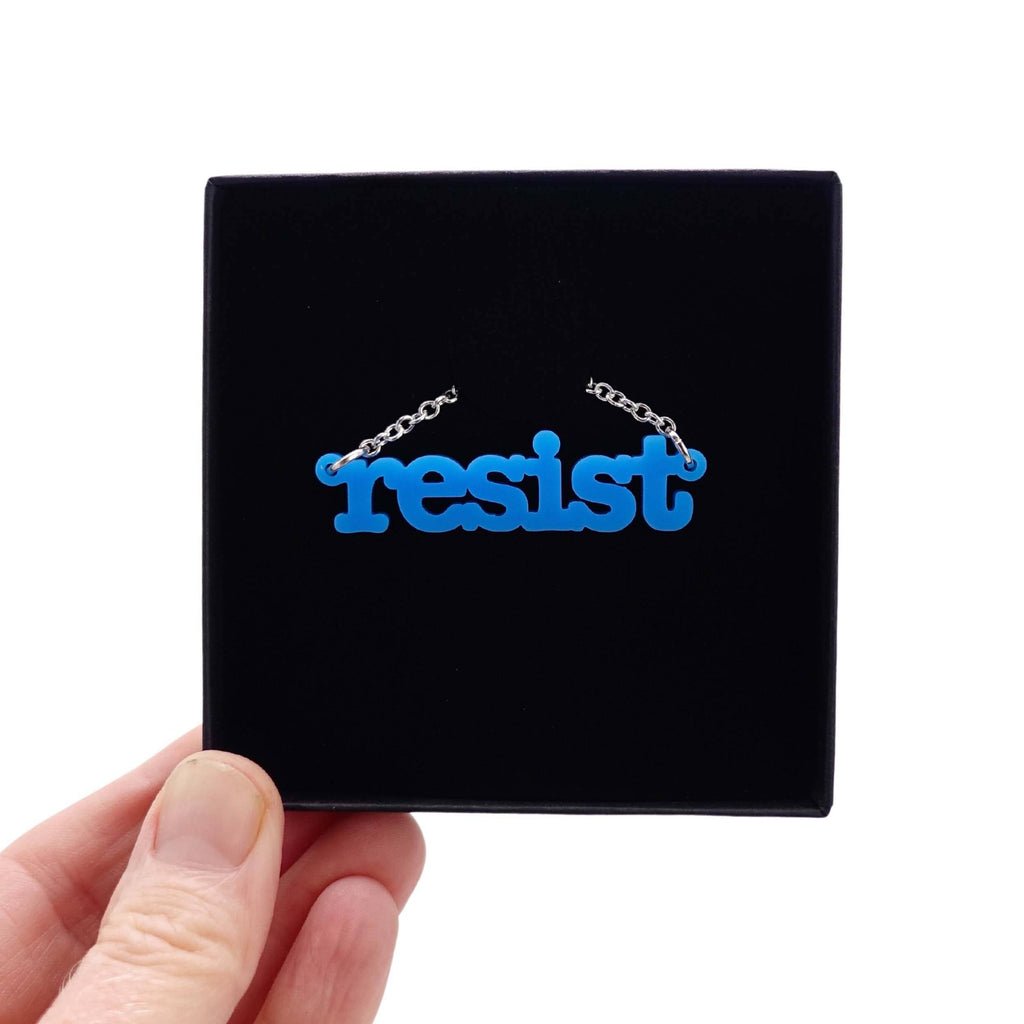 Bright blue Resist necklace in typewriter font shown in a Wear and Resist gift box. 