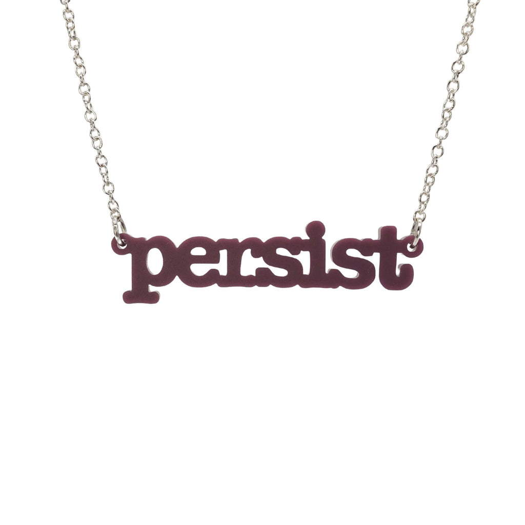 Cassis Persist necklace in typewriter font hanging on a silver chain against a white background. 