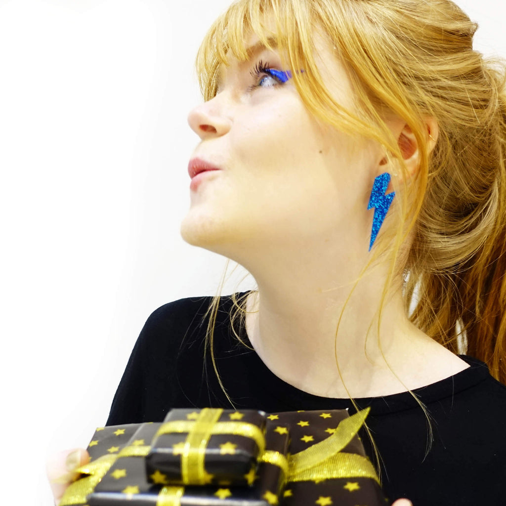 Model wears blue glitter lightning bolt earrings designed by Sarah Day for Wear and Resist. 