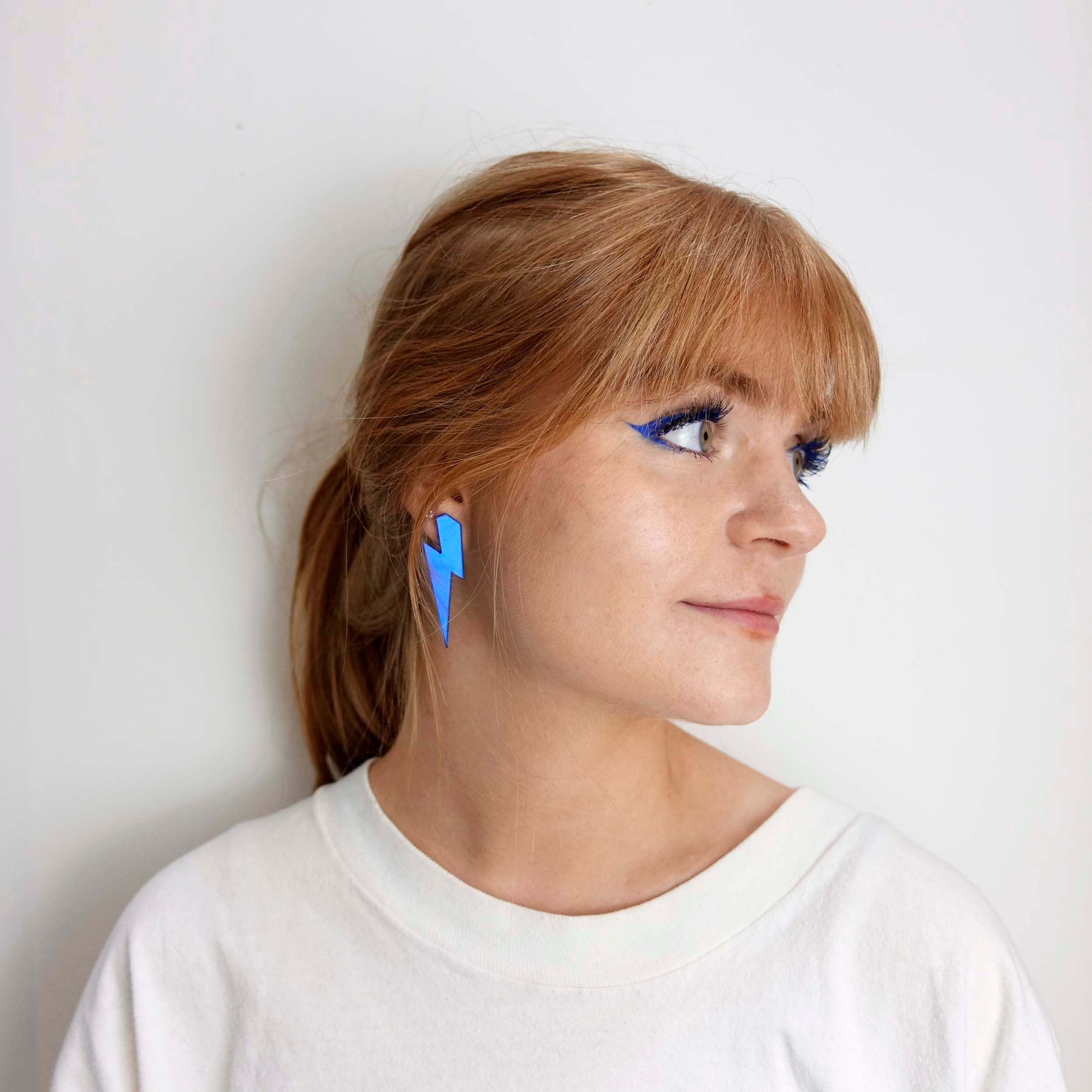Model wears lightning bolt earrings in electric blue mirror. 