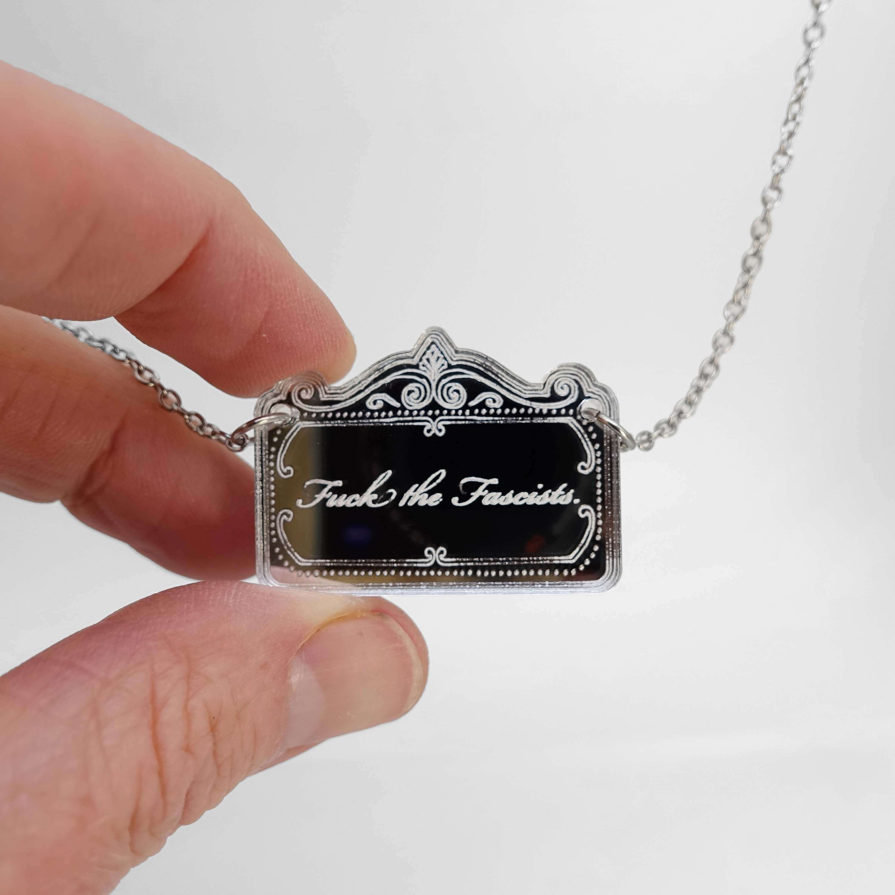 A necklace etched with 'fuck the fascists' held in my hand for scale.