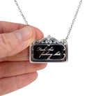 A small necklace etched with 'fuck this fucking shit' shown held by my hand for scale. 