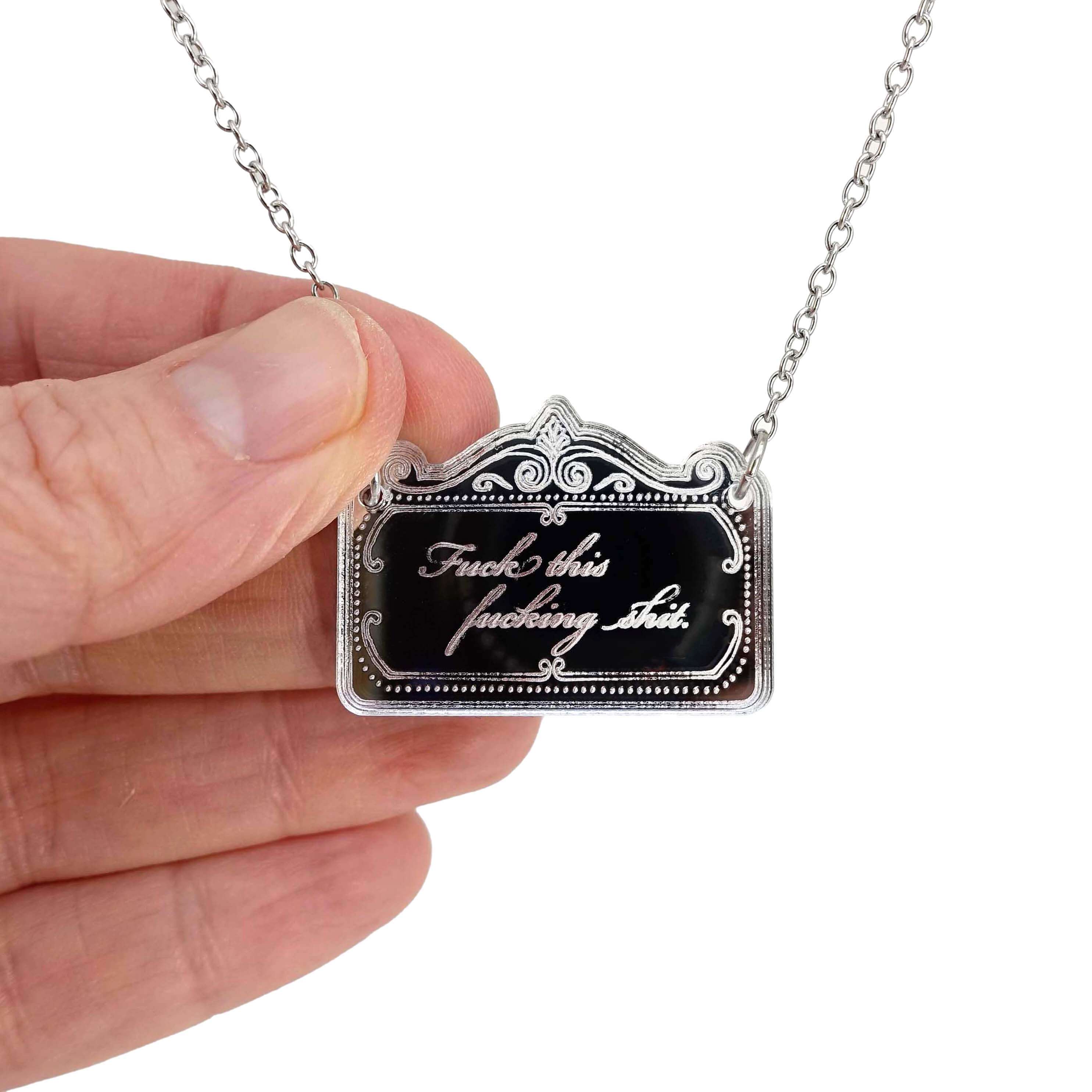 A small necklace etched with 'fuck this fucking shit' shown held by my hand for scale. 