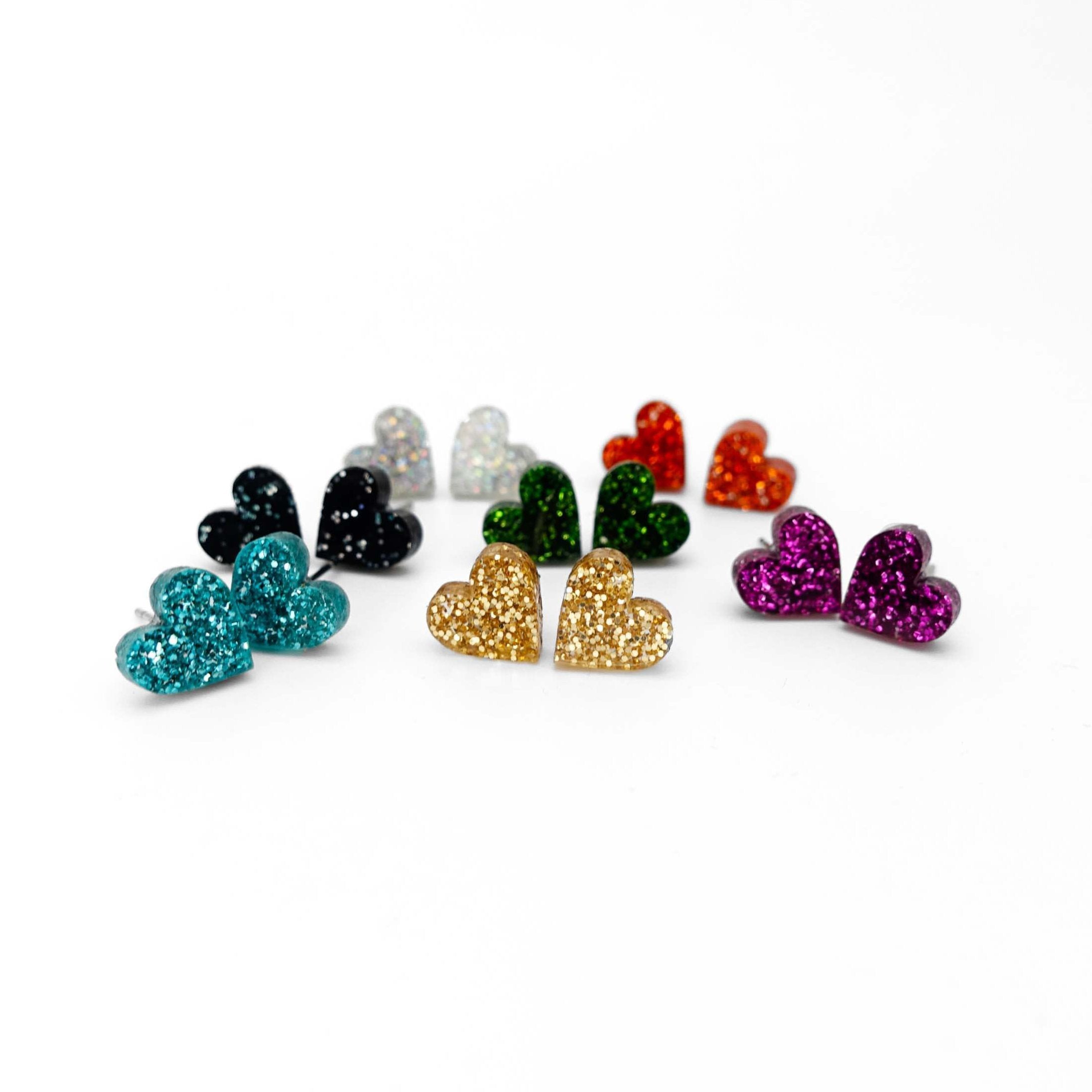 A group shot showing seven pairs of little glitter heart earrings in different colours. 