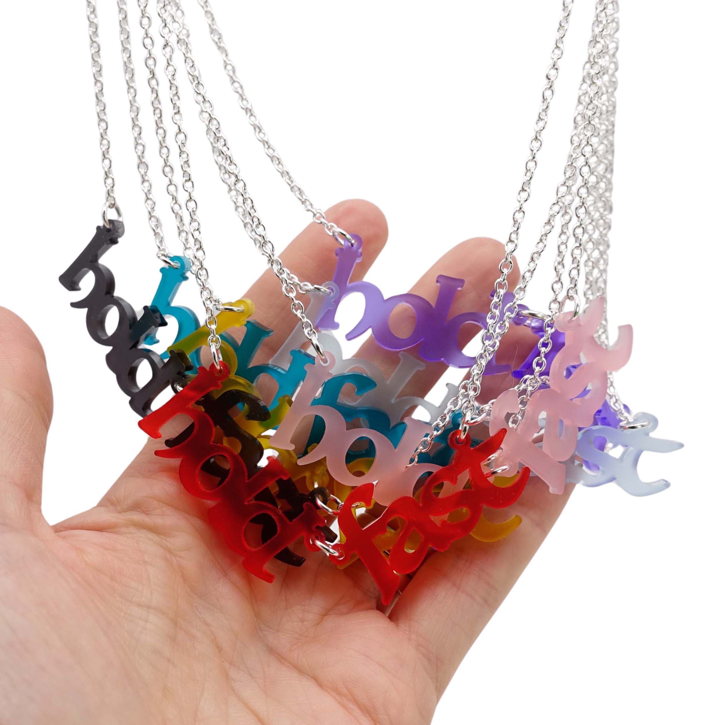 A group of Hold Fast necklaces in seven different frost colours, shown hanging together with a hand for scale. 
