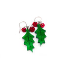 A pair of naturalistic Holly earrings with red berries shown lying on a white surface. 